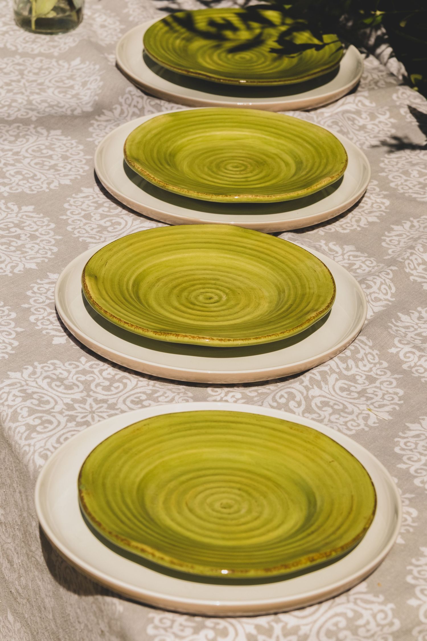 Four green spiral ceramic plates on white floral tablecloth, elegant table setting.