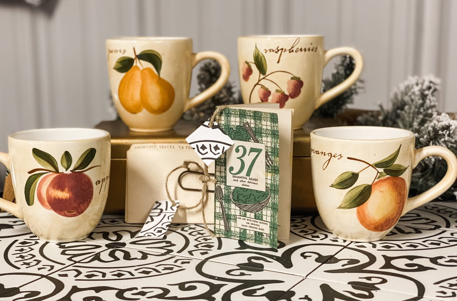 Vintage-style ceramic mugs with hand-painted fruit designs arranged on black and white patterned tablecloth.