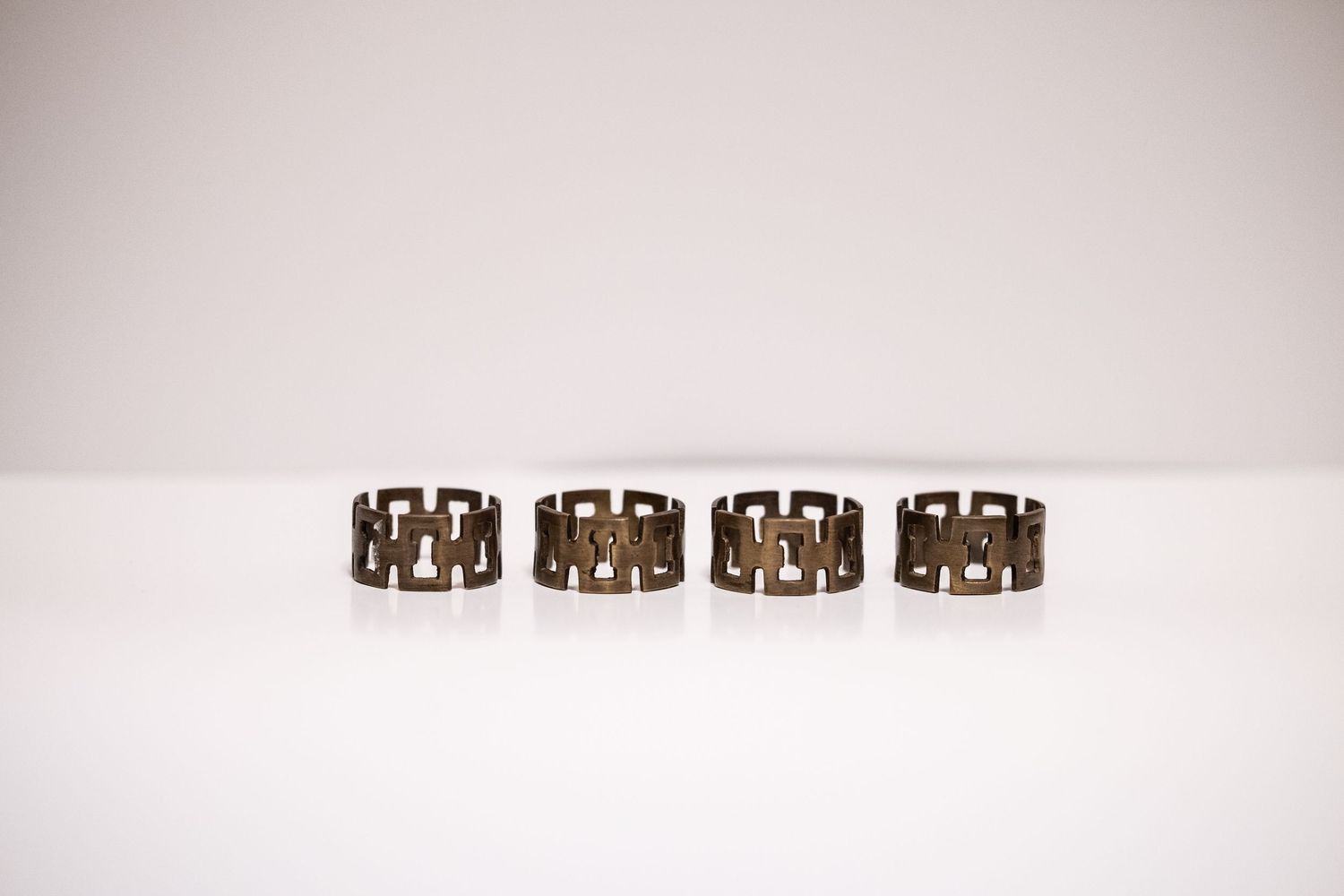 Set of four vintage brass geometric napkin rings with interlocking square pattern design on white surface.