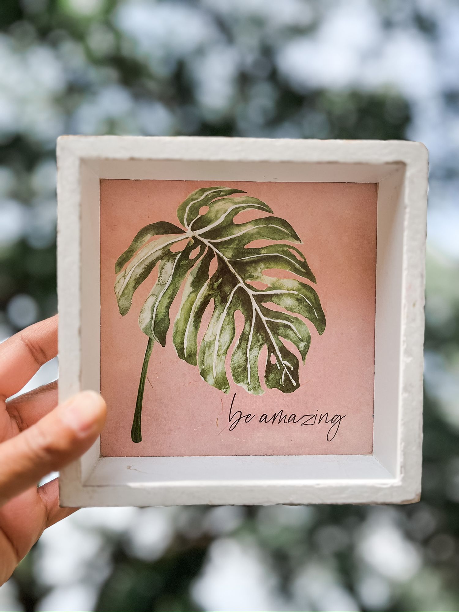 Framed watercolor monstera leaf artwork with 'be amazing' text on pink background.
