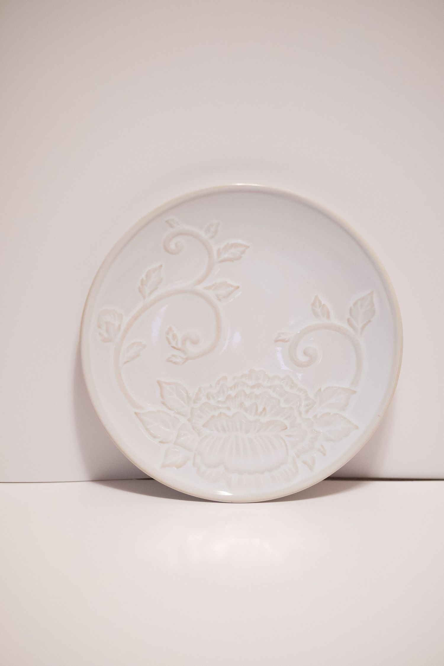 White ceramic plate with embossed floral and vine design, standing upright against a white background.