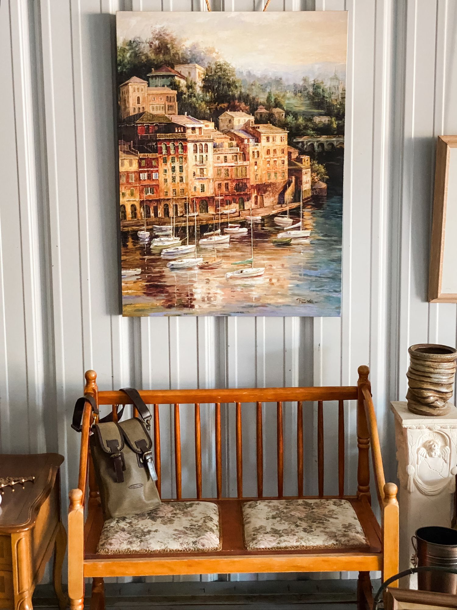 Mediterranean coastal town painting displayed above a wooden bench in a rustic interior setting.