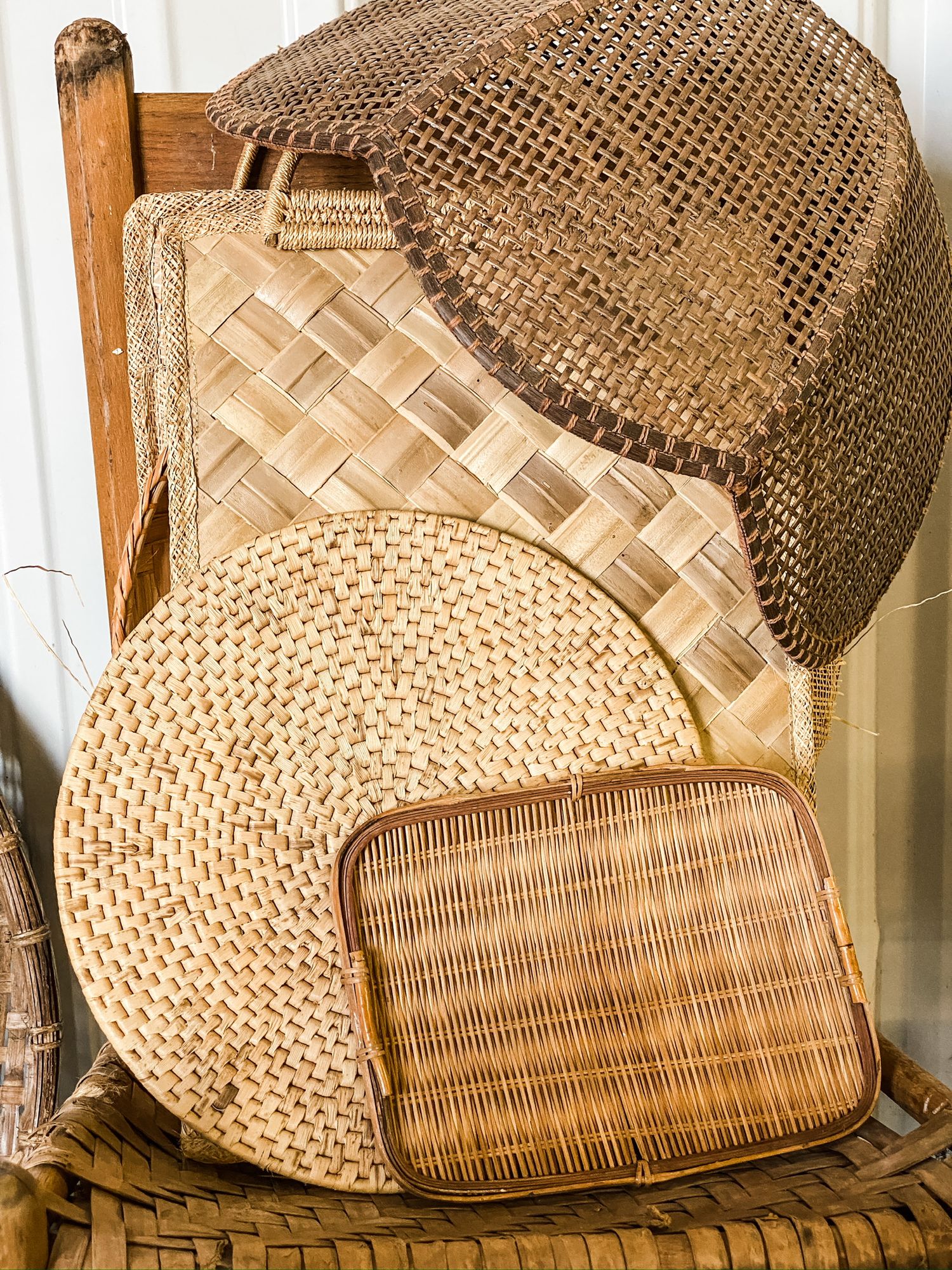 Collection of natural woven baskets and placemats in neutral tones stacked on wooden chair.