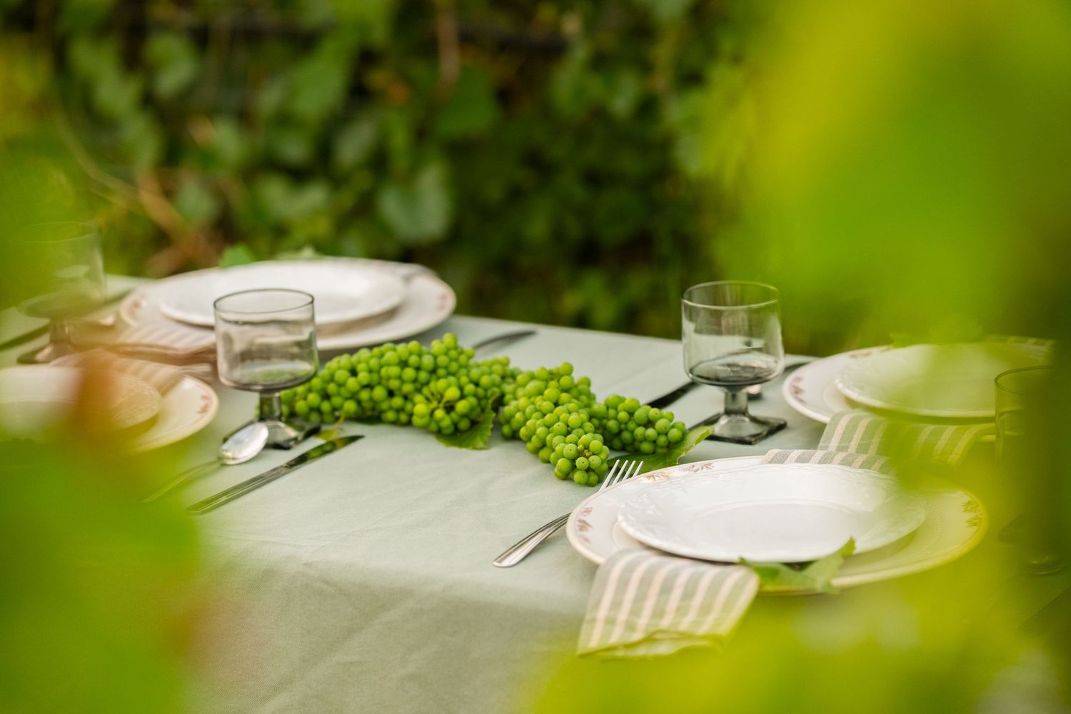 Elegant outdoor table setting with green grape centerpiece, white plates, and glassware on a linen tablecloth.