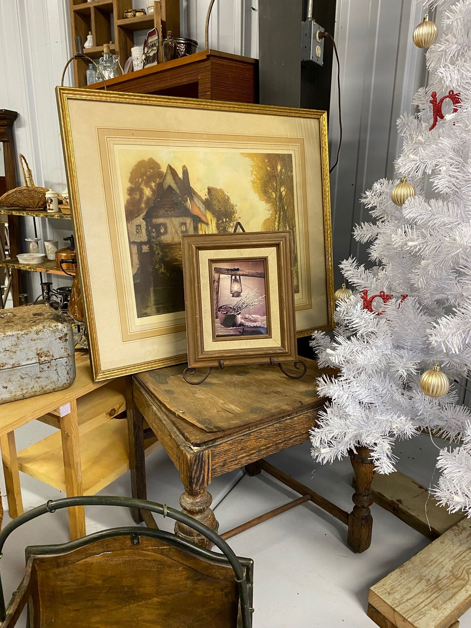Vintage framed artwork and white Christmas tree displayed on antique wooden furniture.