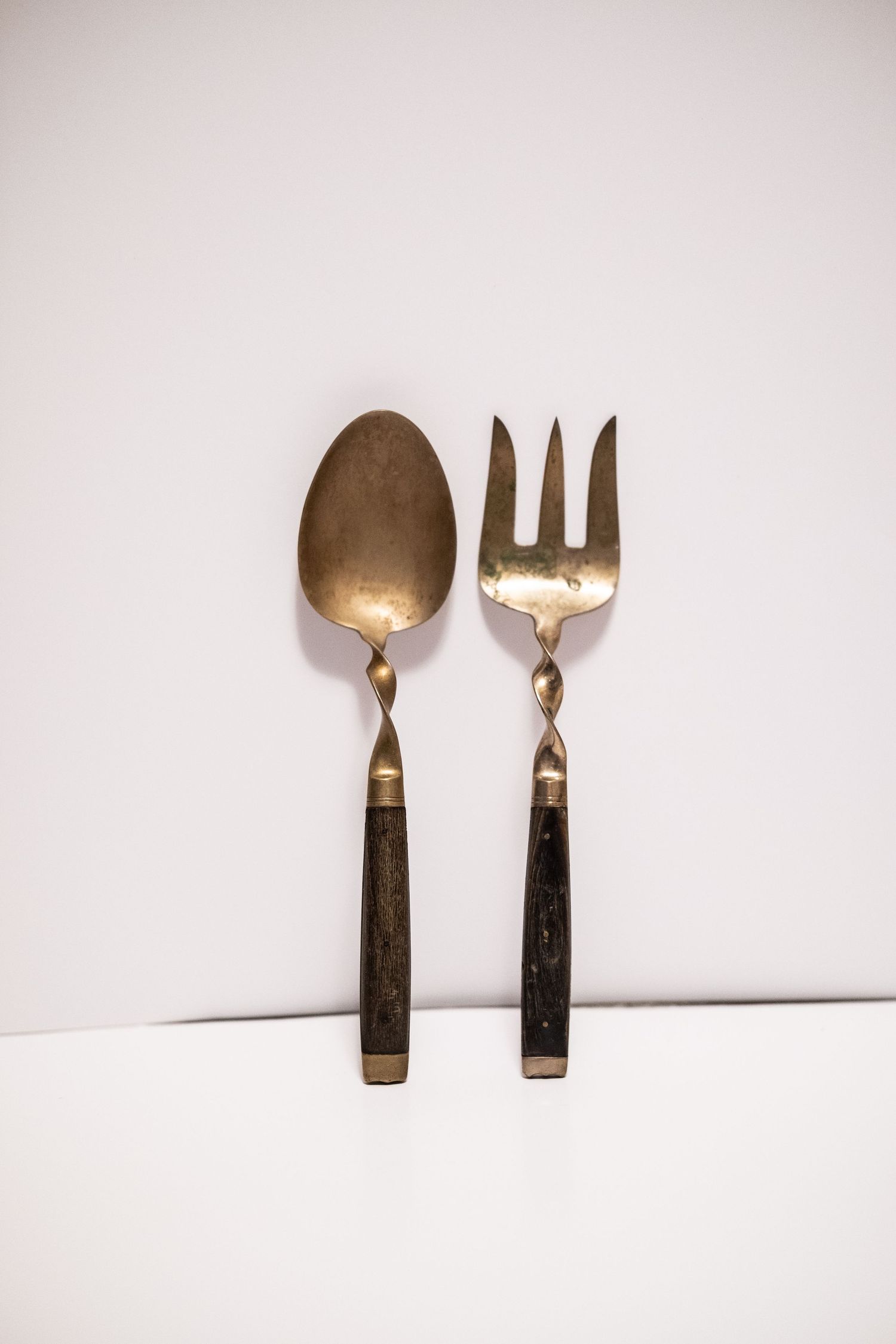 Antique brass spoon and fork set with dark wooden handles on white background.