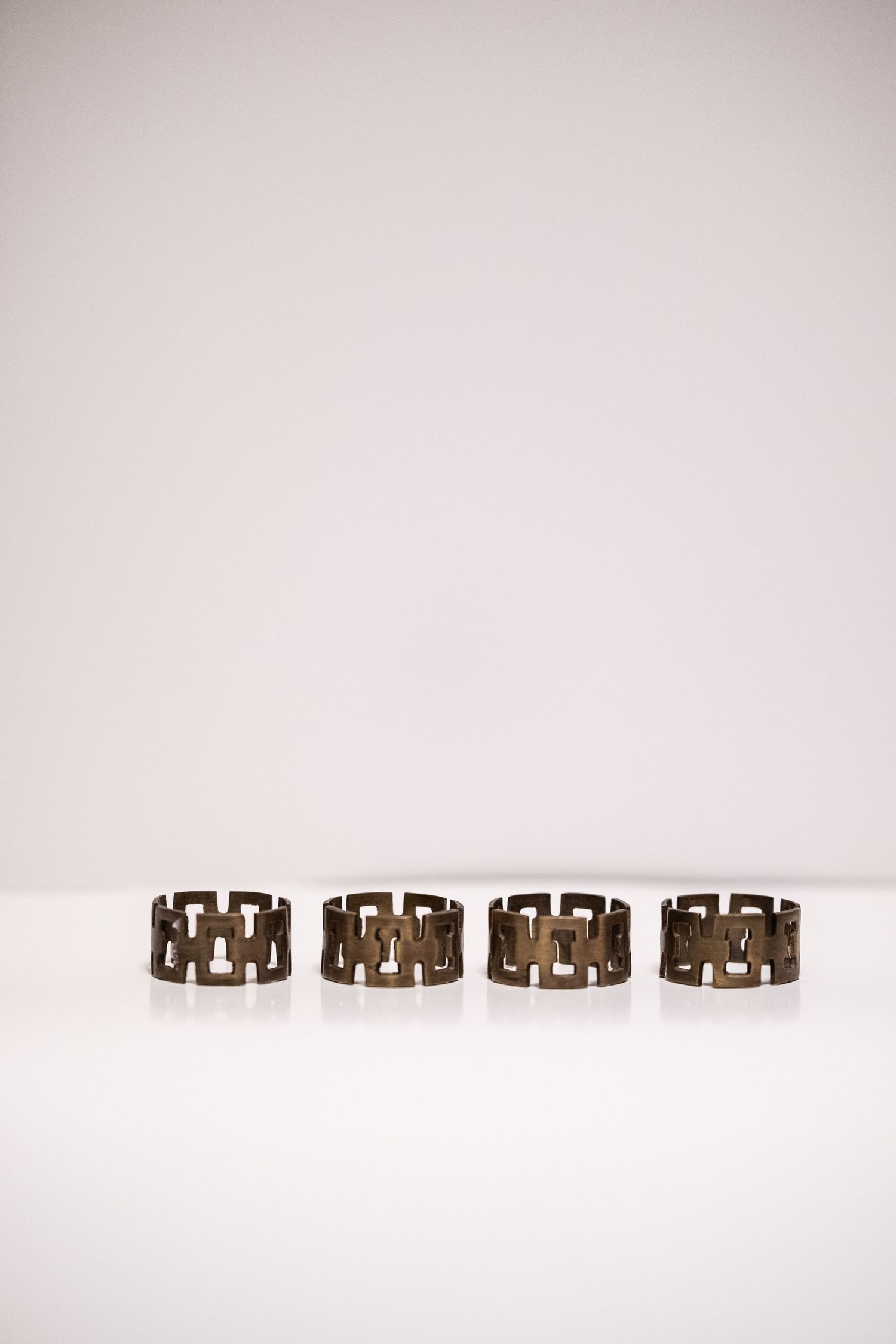 Set of four antique bronze geometric chain-link napkin rings displayed in a row on a white surface.