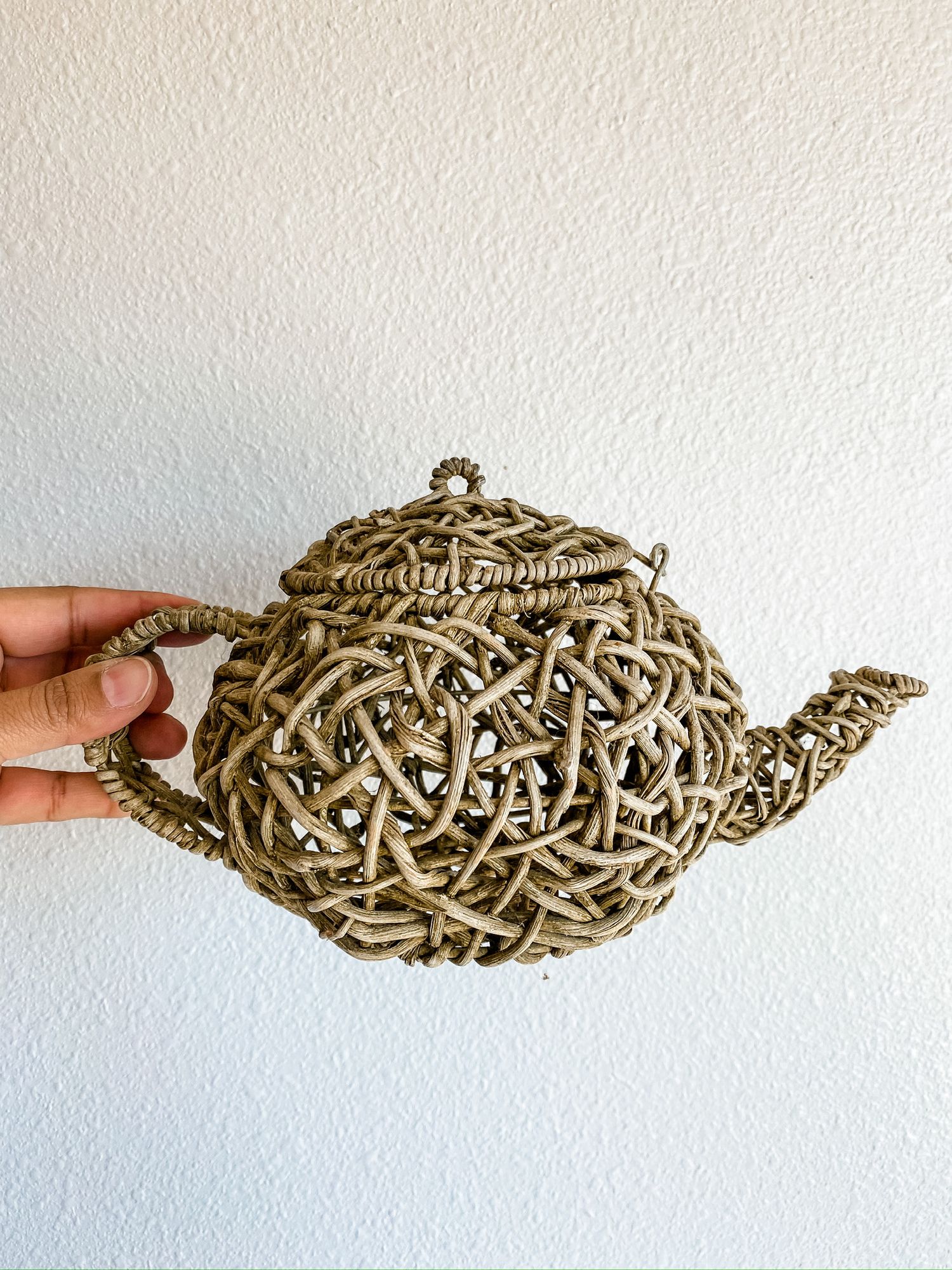 Decorative teapot made entirely of woven natural twigs or branches against white background.