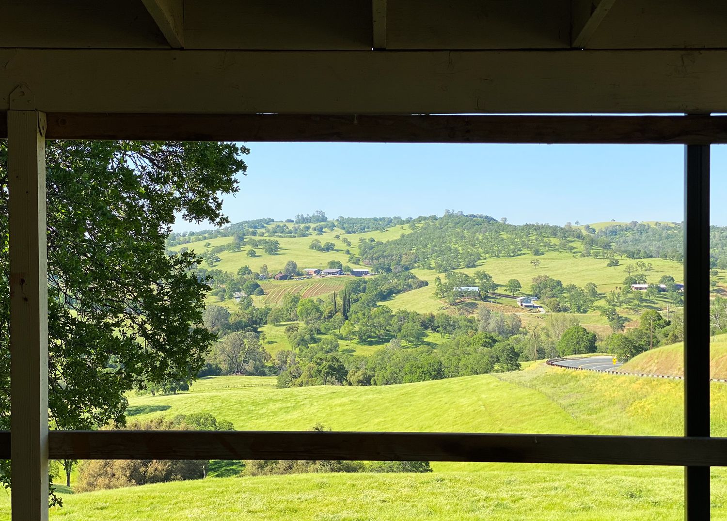 Rolling green hills and countryside viewed through a rustic covered porch frame.