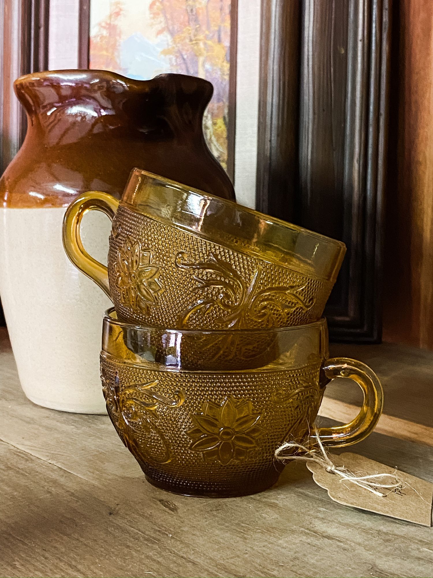 Two amber glass cups with embossed patterns stacked in front of a brown ceramic jug.