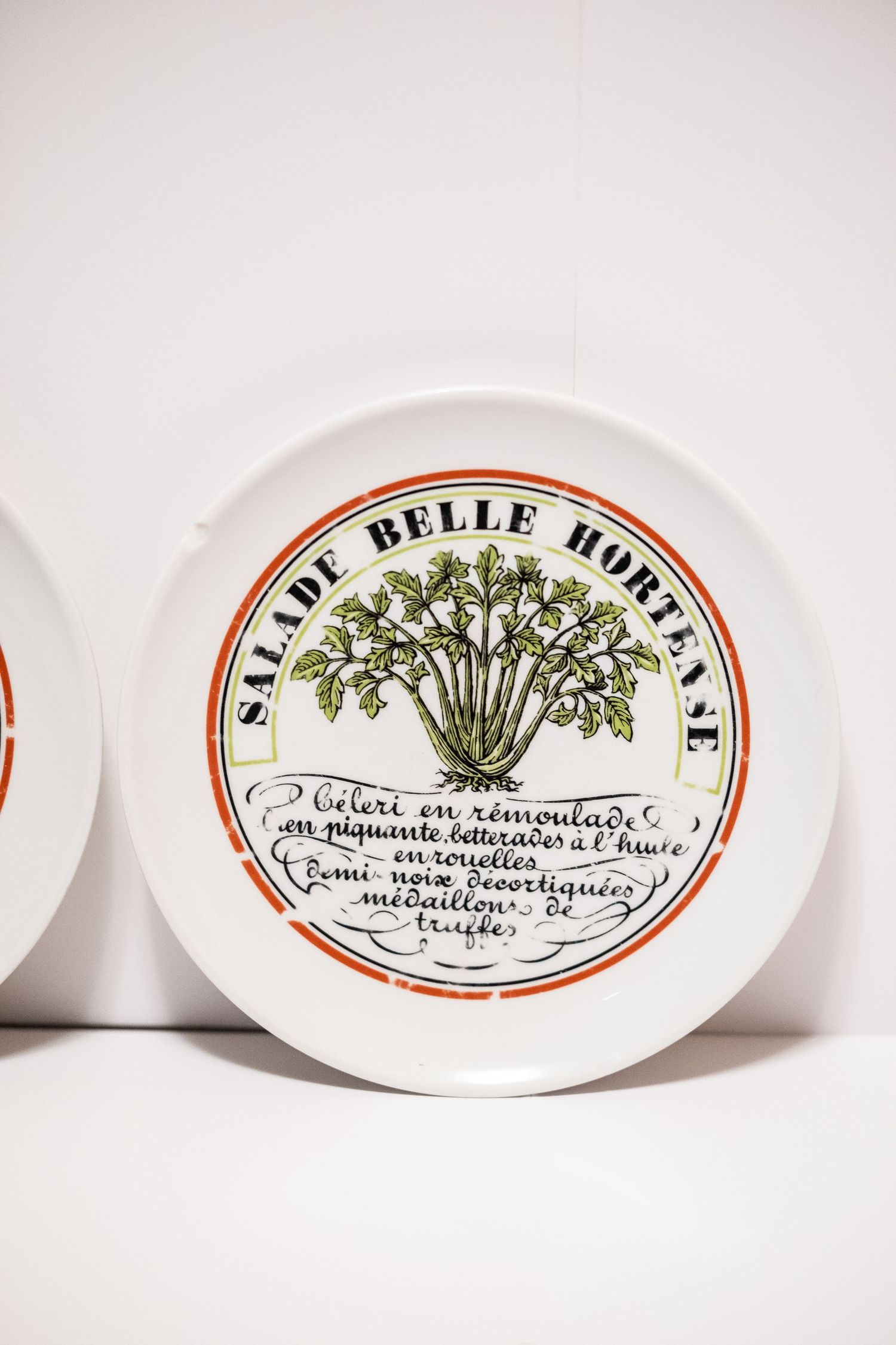 White ceramic plate with French text reading Salade Belle Hortense, featuring illustrated green herbs and cursive writing.