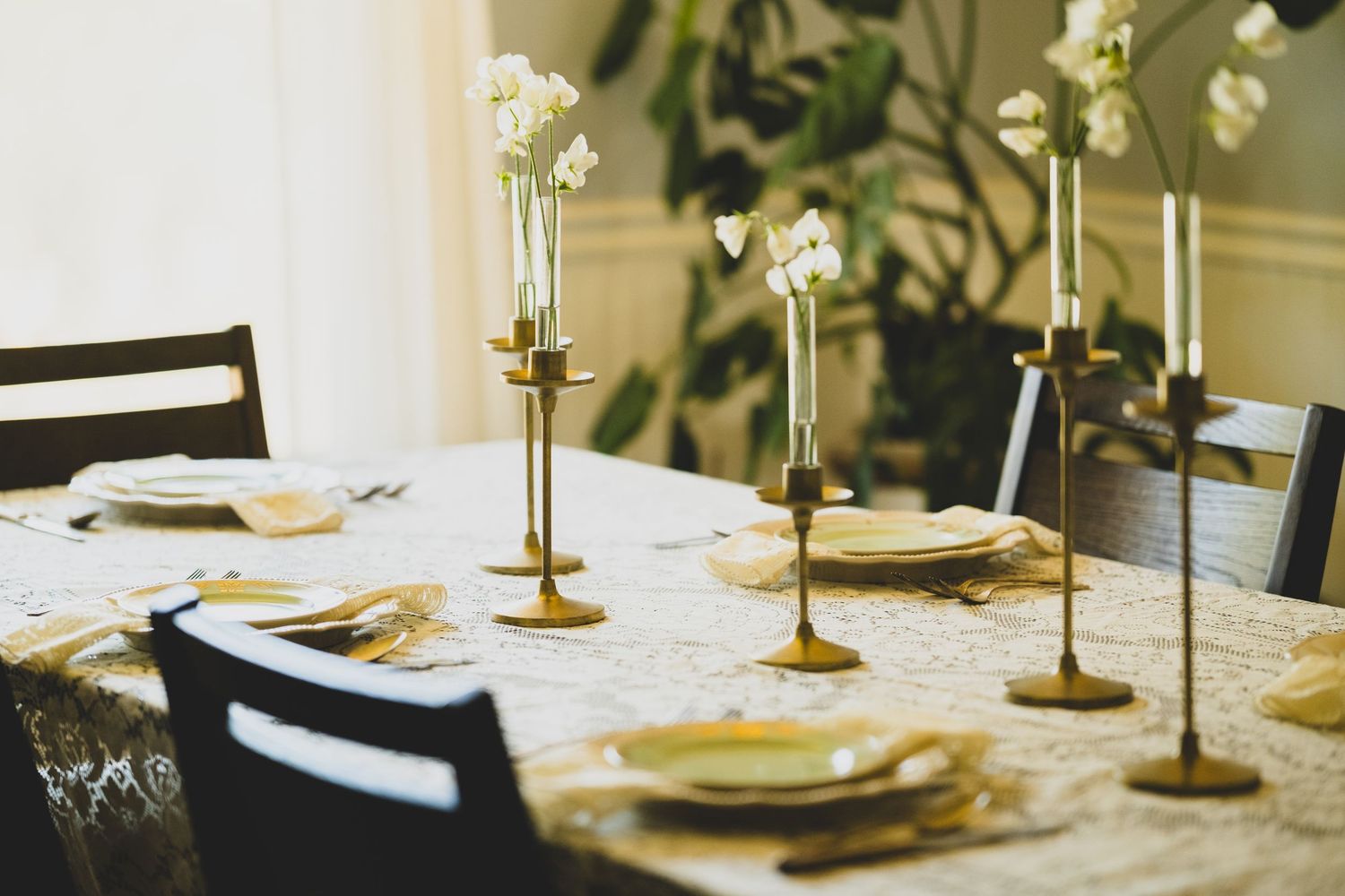 Elegant dining table set with gold candlesticks, white orchids, and gold cutlery on a lace tablecloth.