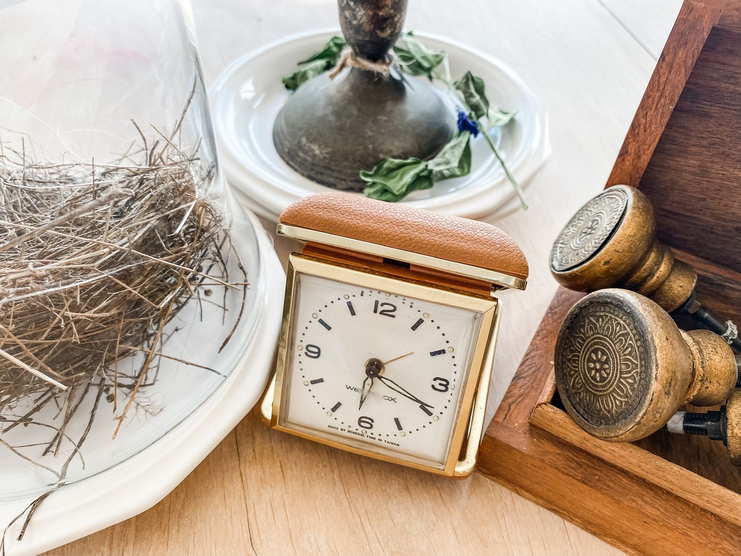 Vintage alarm clock and decorative items arranged on wooden surface with greenery.