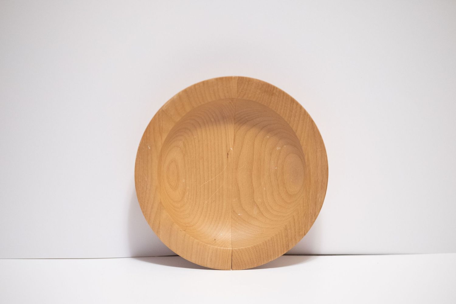 Round wooden bowl with natural cherry wood grain finish, leaning against white background.