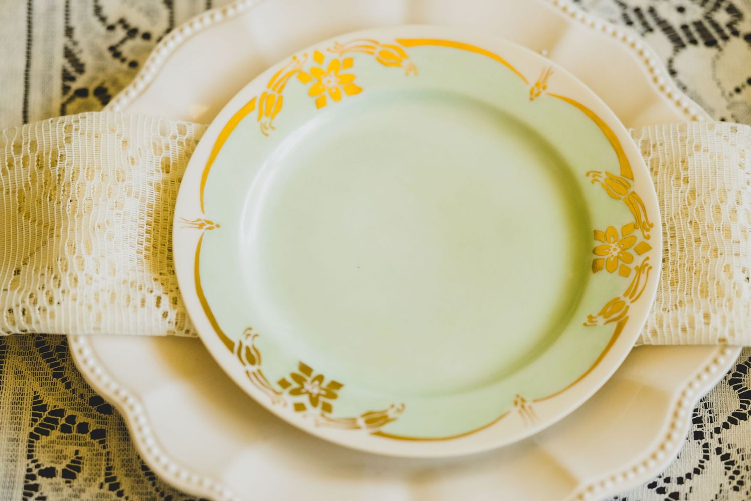Vintage green plate with gold floral border on white lace tablecloth, elegant antique dinnerware setting.