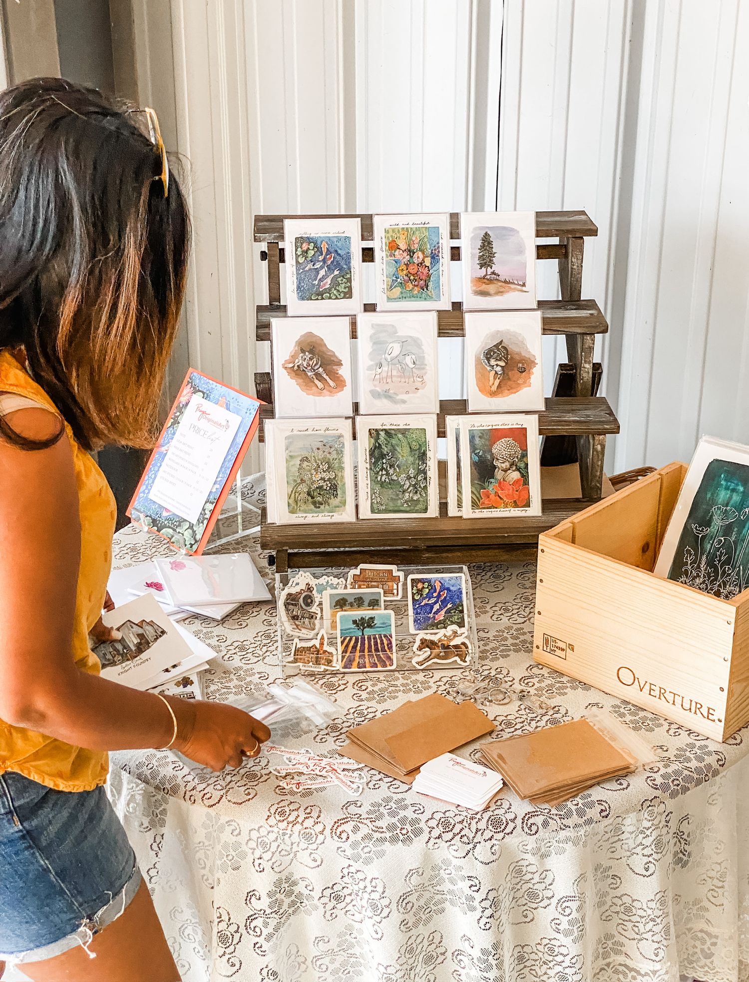 Display of artistic greeting cards and prints arranged on a wooden stand at a craft market table.