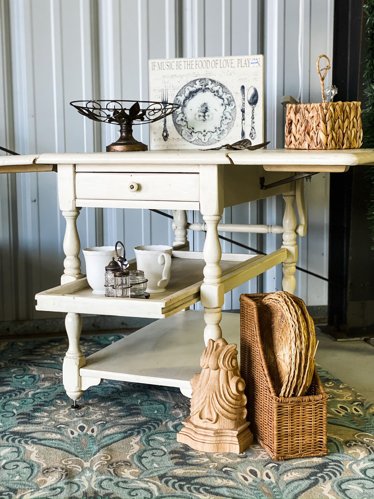 Vintage white tiered table styled with decorative accessories and woven baskets on a patterned rug.