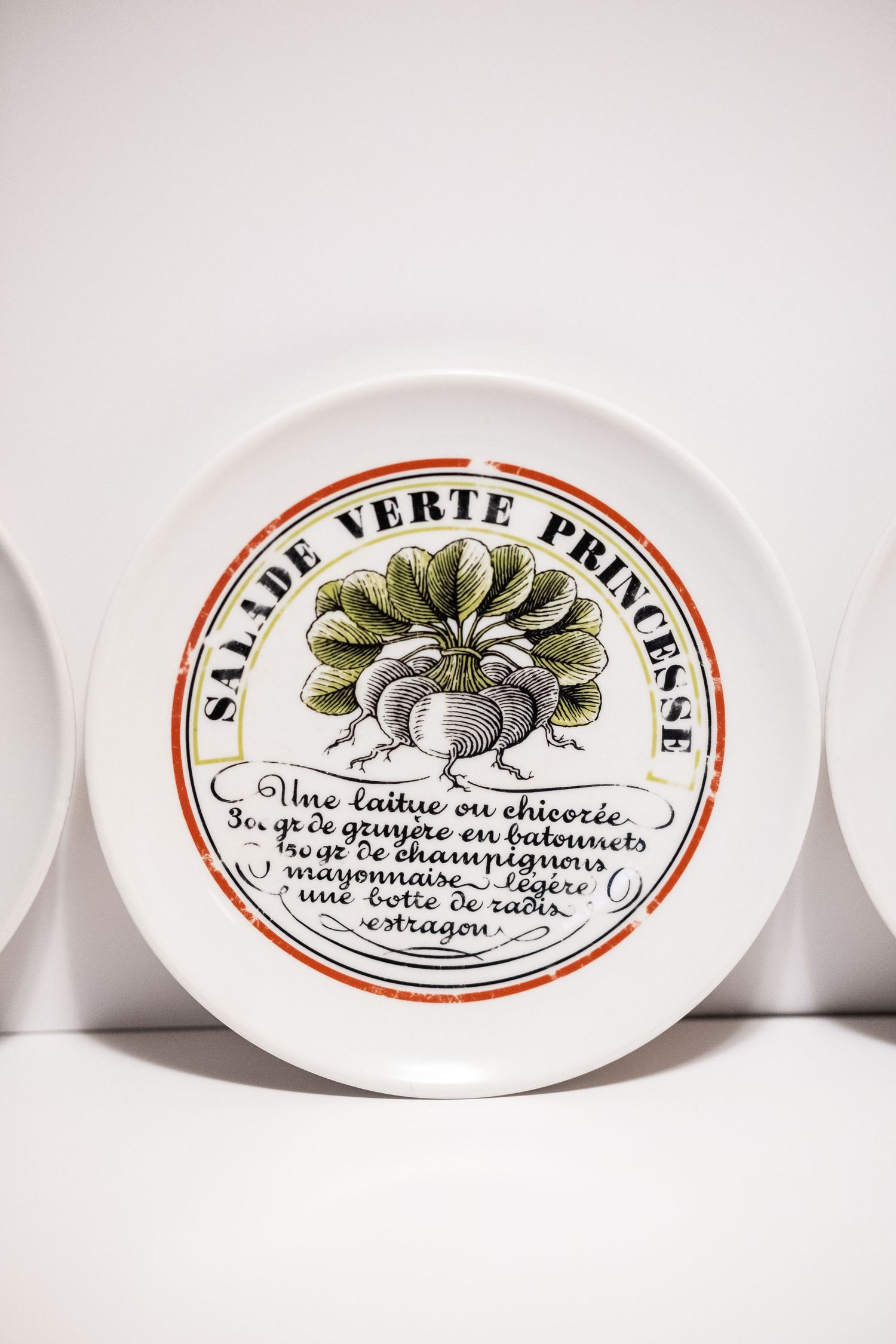 Vintage French ceramic plate with Salade Verte Princesse recipe and radish illustration, displayed on white shelf.