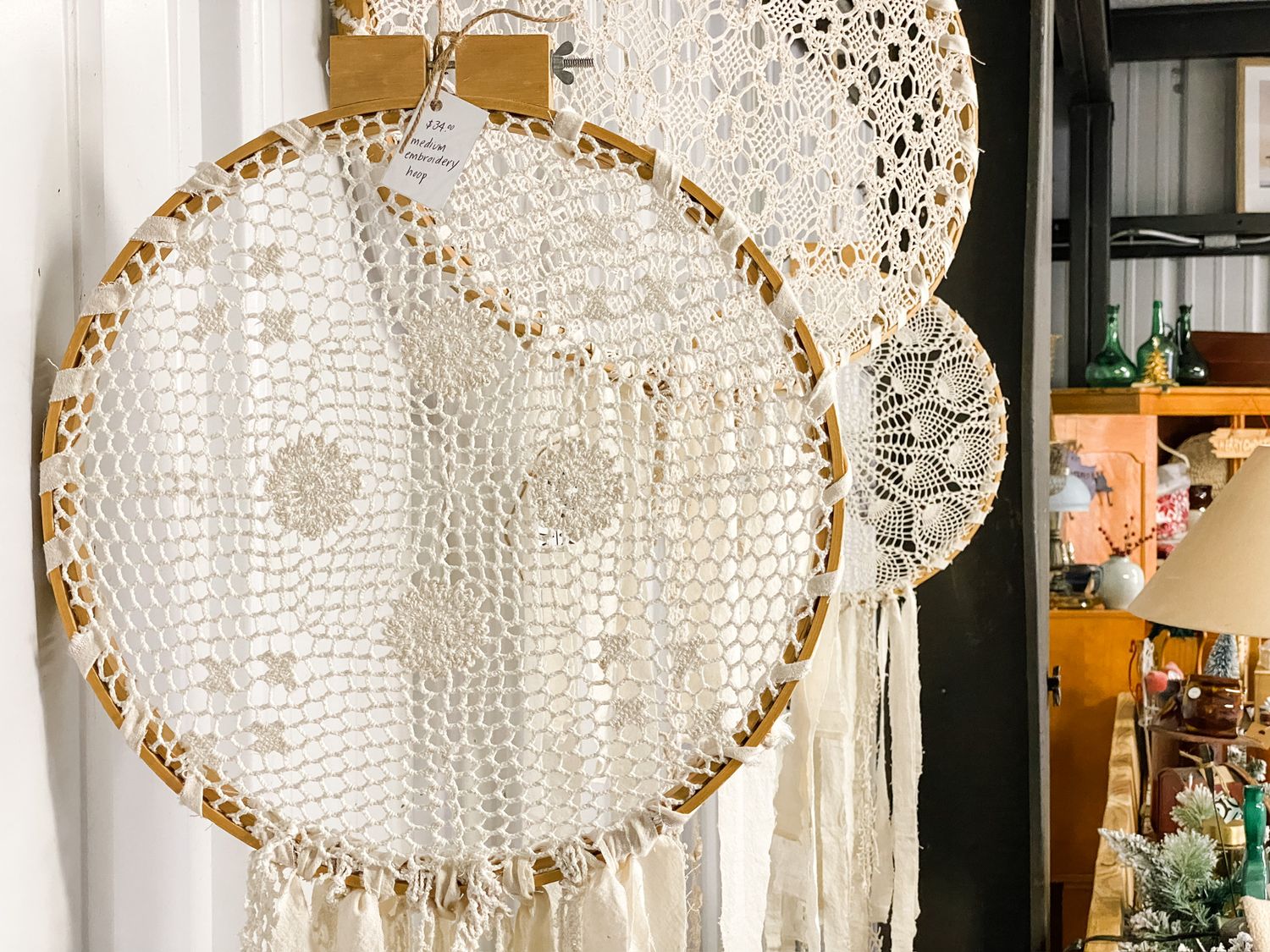 Decorative crochet dreamcatcher with lace and fringe details hanging on a wall.