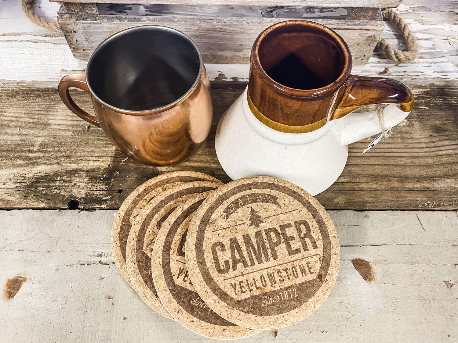Copper and white ceramic coffee mugs with wooden Camper coasters on rustic table.