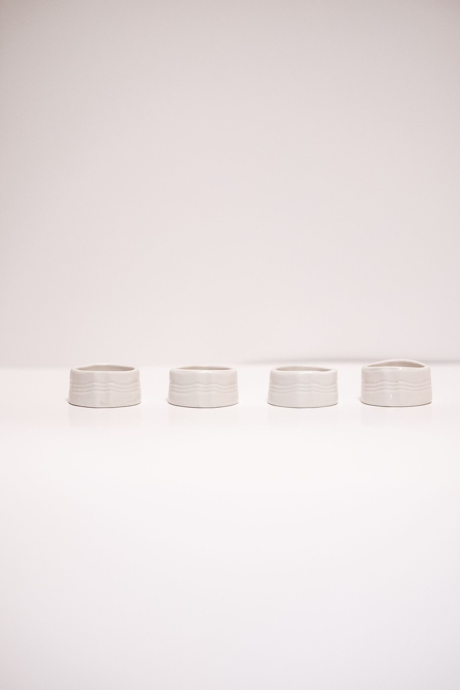 Set of four white ceramic ribbed napkin rings arranged in a row on a white surface.