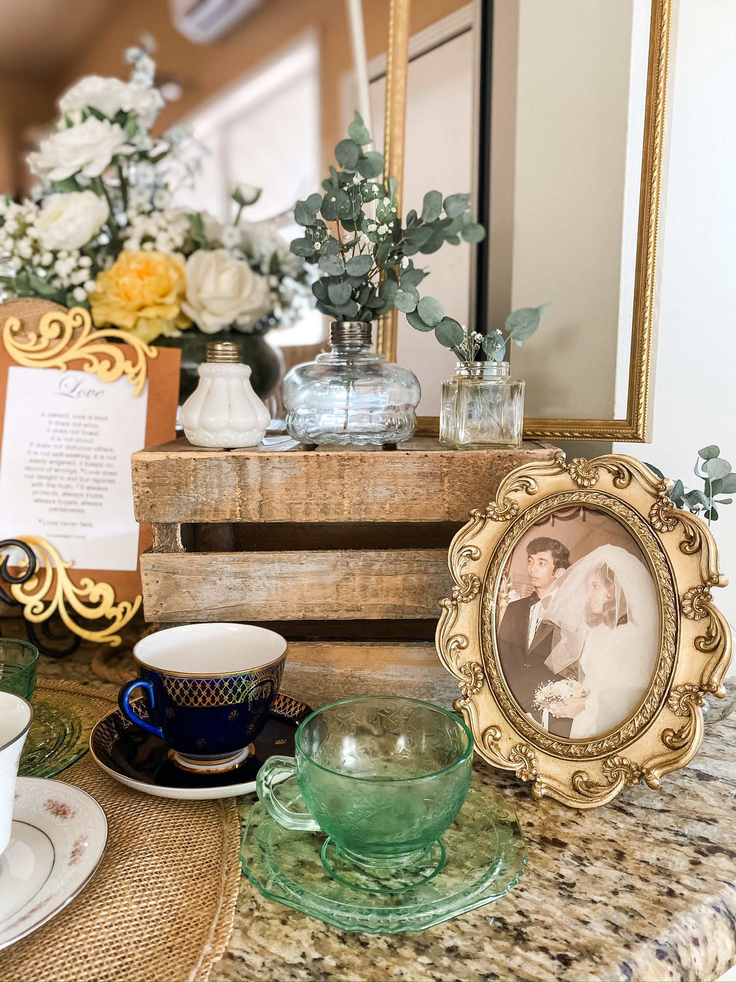 Elegant tea setting with floral arrangements, vintage teacups, and ornate picture frame on burlap tablecloth.