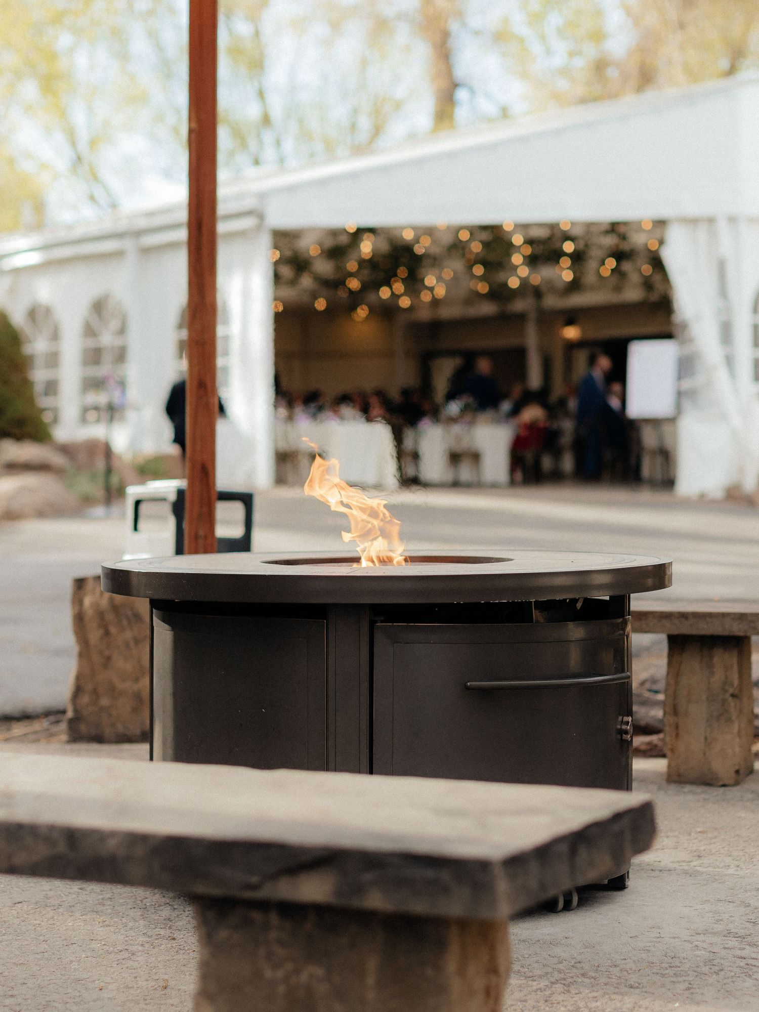 Outdoor fire pit table glowing at dusk outside elegant tented wedding reception.