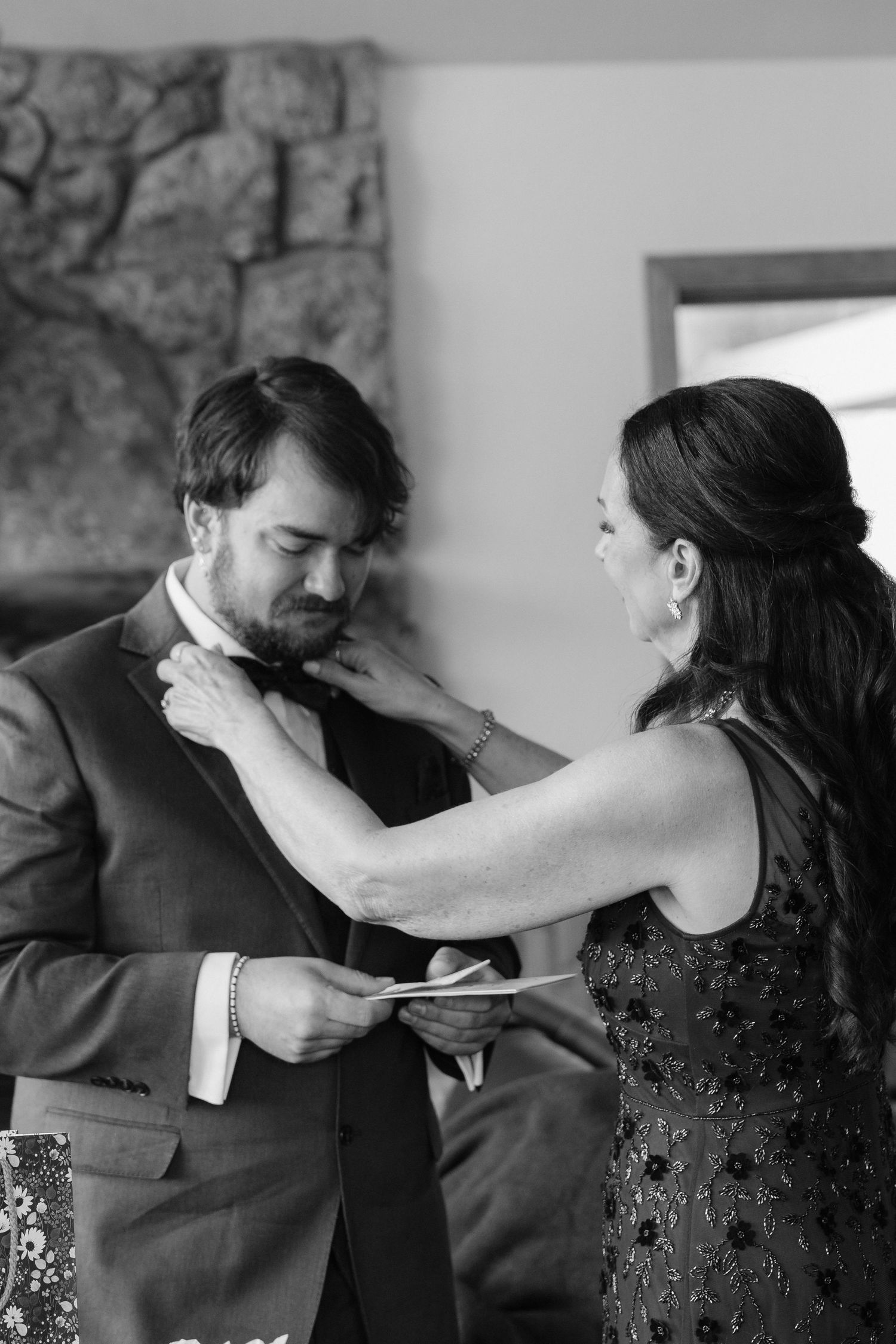 Black and white photo of a woman adjusting a grooms bow tie before a wedding ceremony.