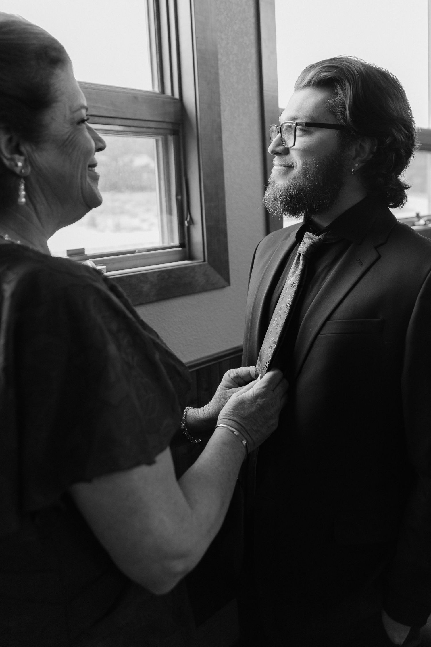 Black and white photo of a mother adjusting her son's tie before his wedding ceremony.