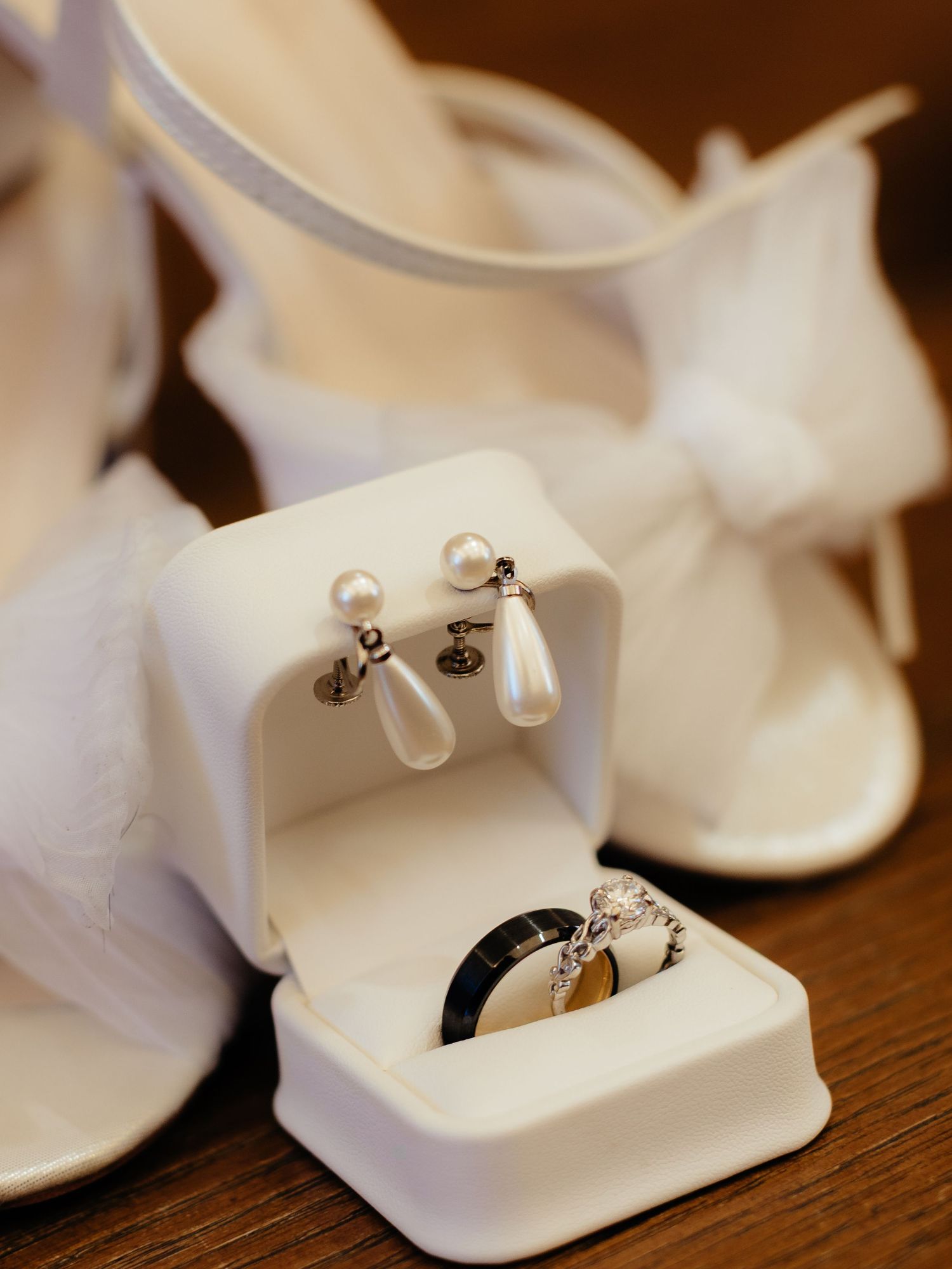 White wedding jewelry box with pearl drop earrings and diamond ring, displayed near bridal heels with bow detail.
