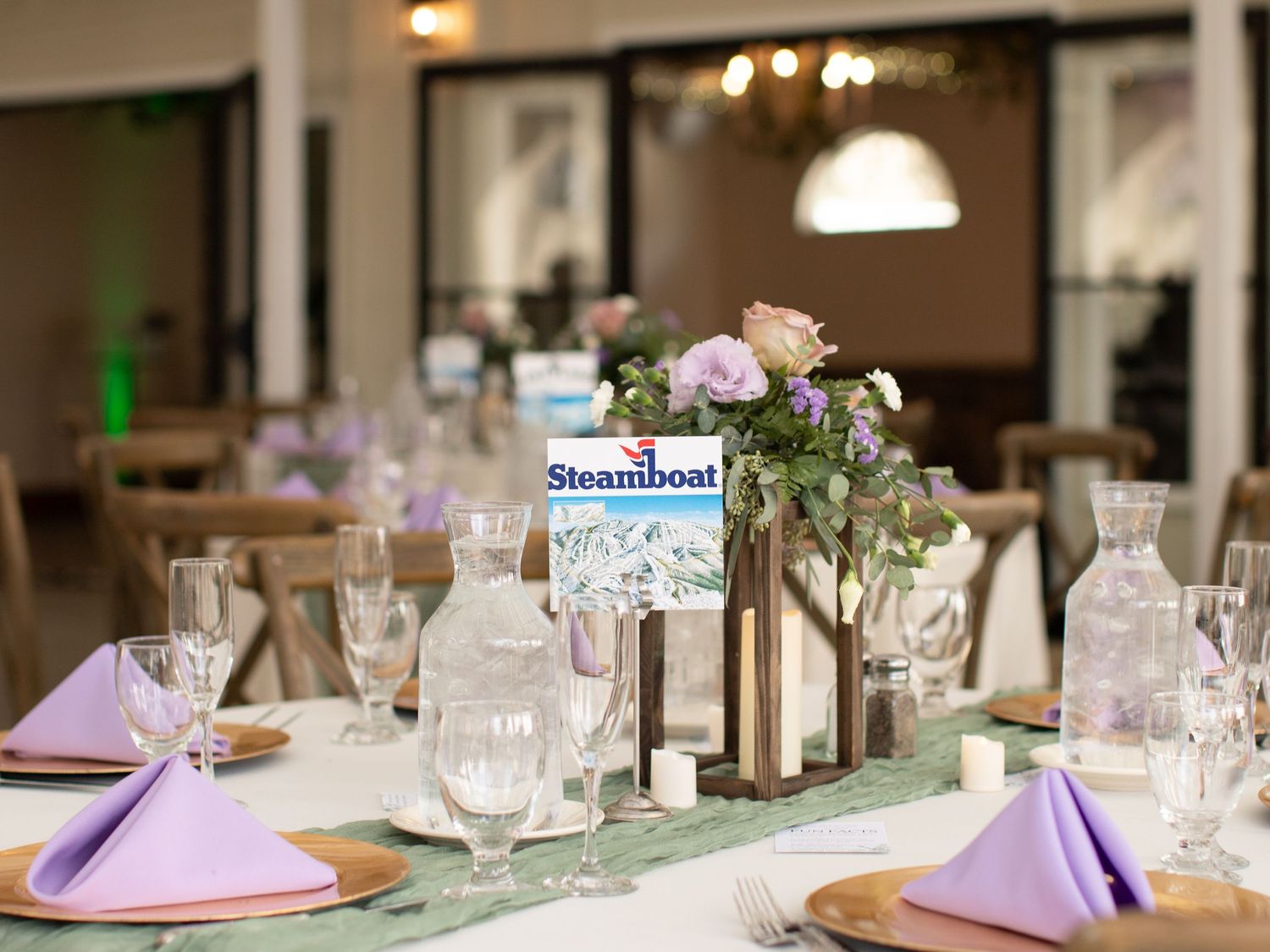 Elegant wedding reception table set with lavender napkins, floral centerpiece, and Steamboat sign.