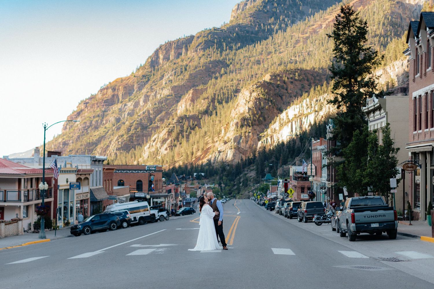 A bride and groom kiss in the middle of a mountain town street in Colorado, with stunning rocky peaks in the background.