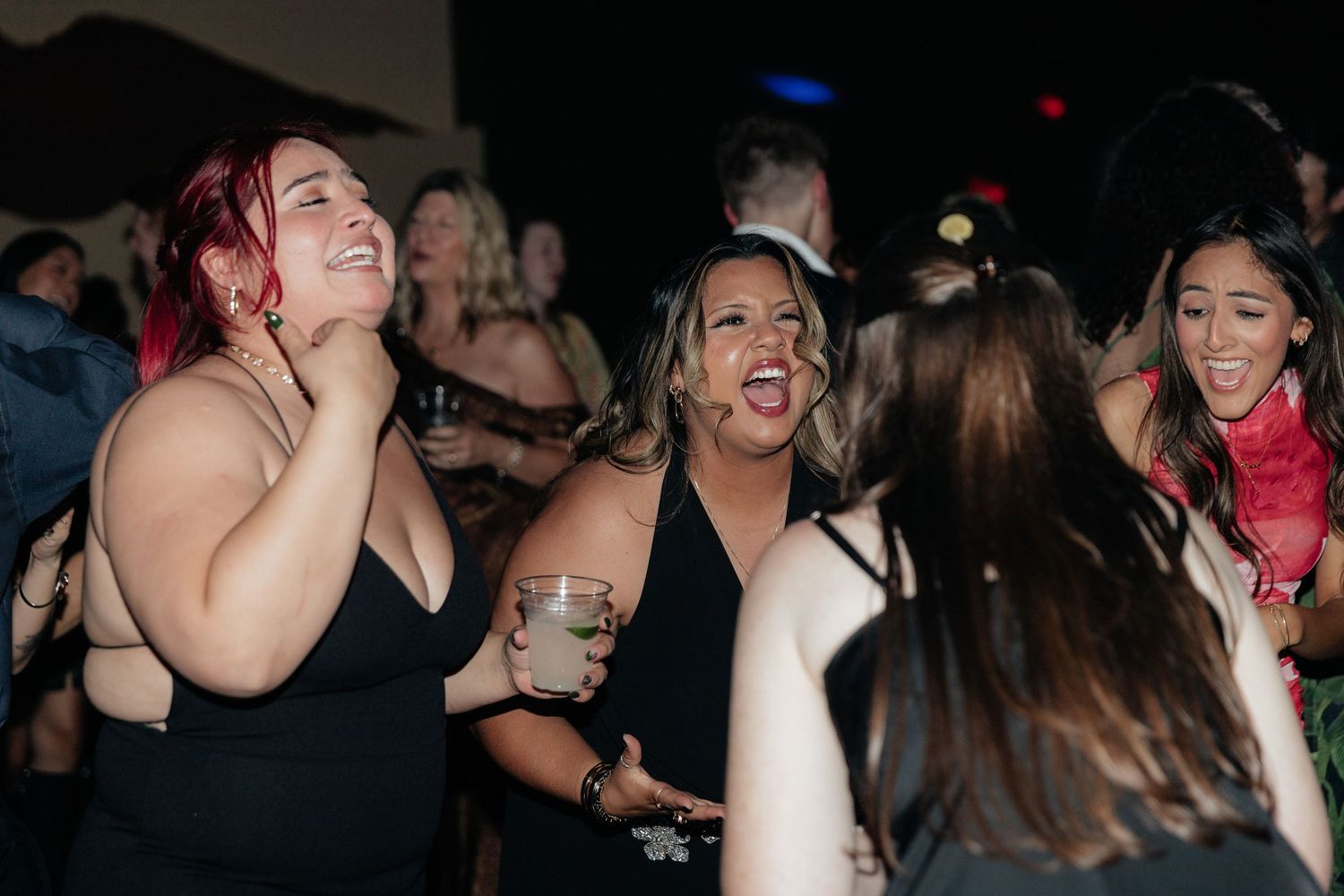 Women laughing and dancing together at lively wedding reception party in dark venue.