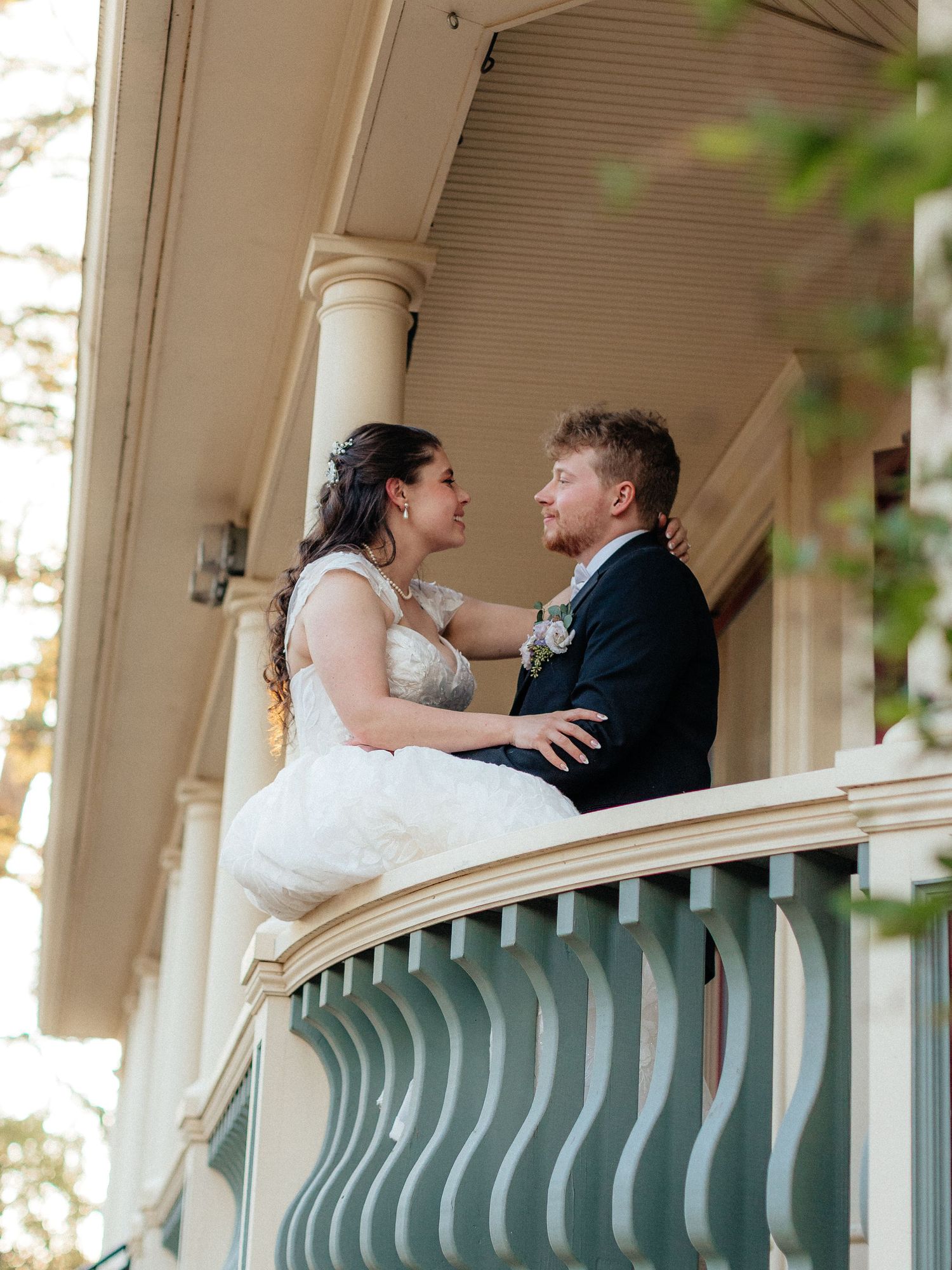 Bride and groom share a romantic moment on a decorative balcony of a historic Victorian venue on their wedding day.