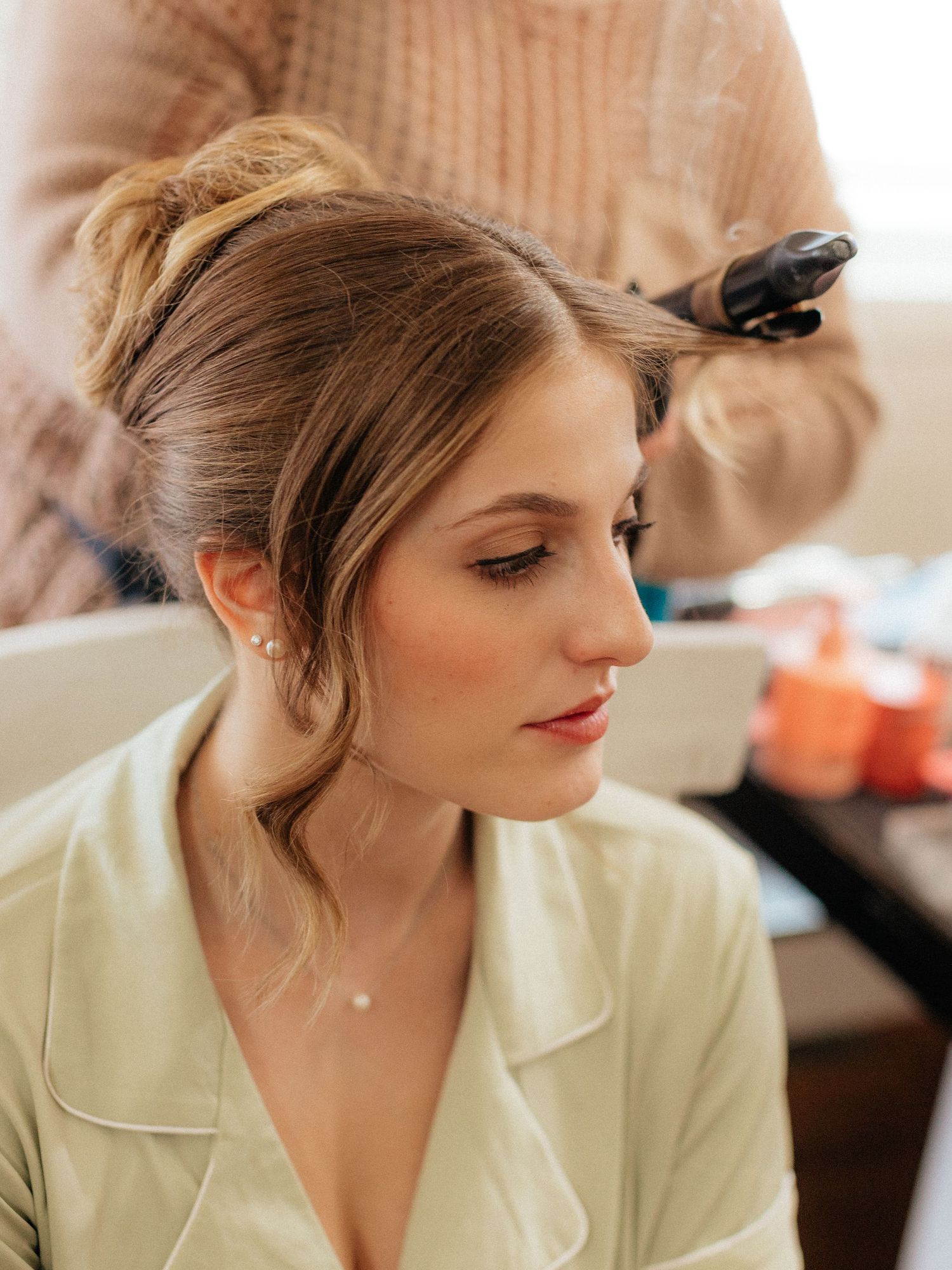 Bride getting her hair styled in an elegant updo with wispy bangs before her wedding day.