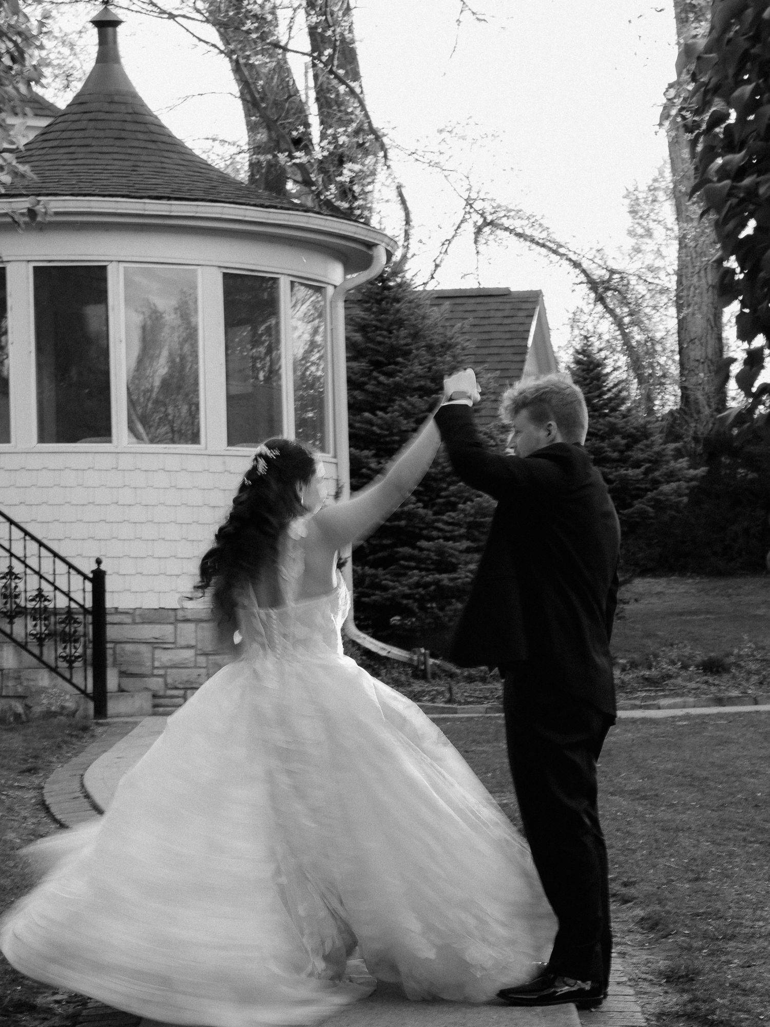 Black and white photo of a bride and groom dancing outdoors near a gazebo on their wedding day.