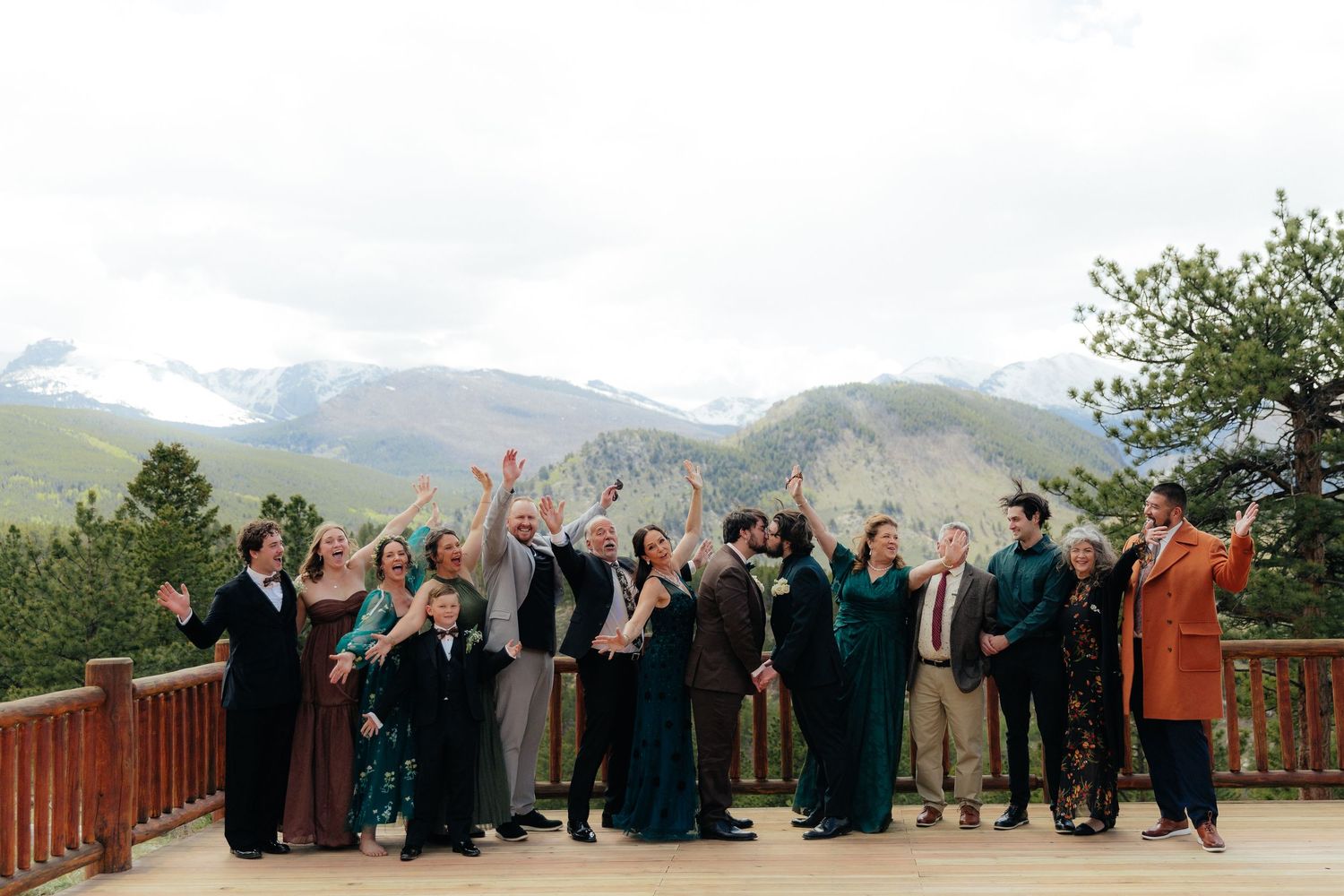 Wedding party celebrating on a mountain deck with stunning Rocky Mountain peaks and evergreen trees in the background.