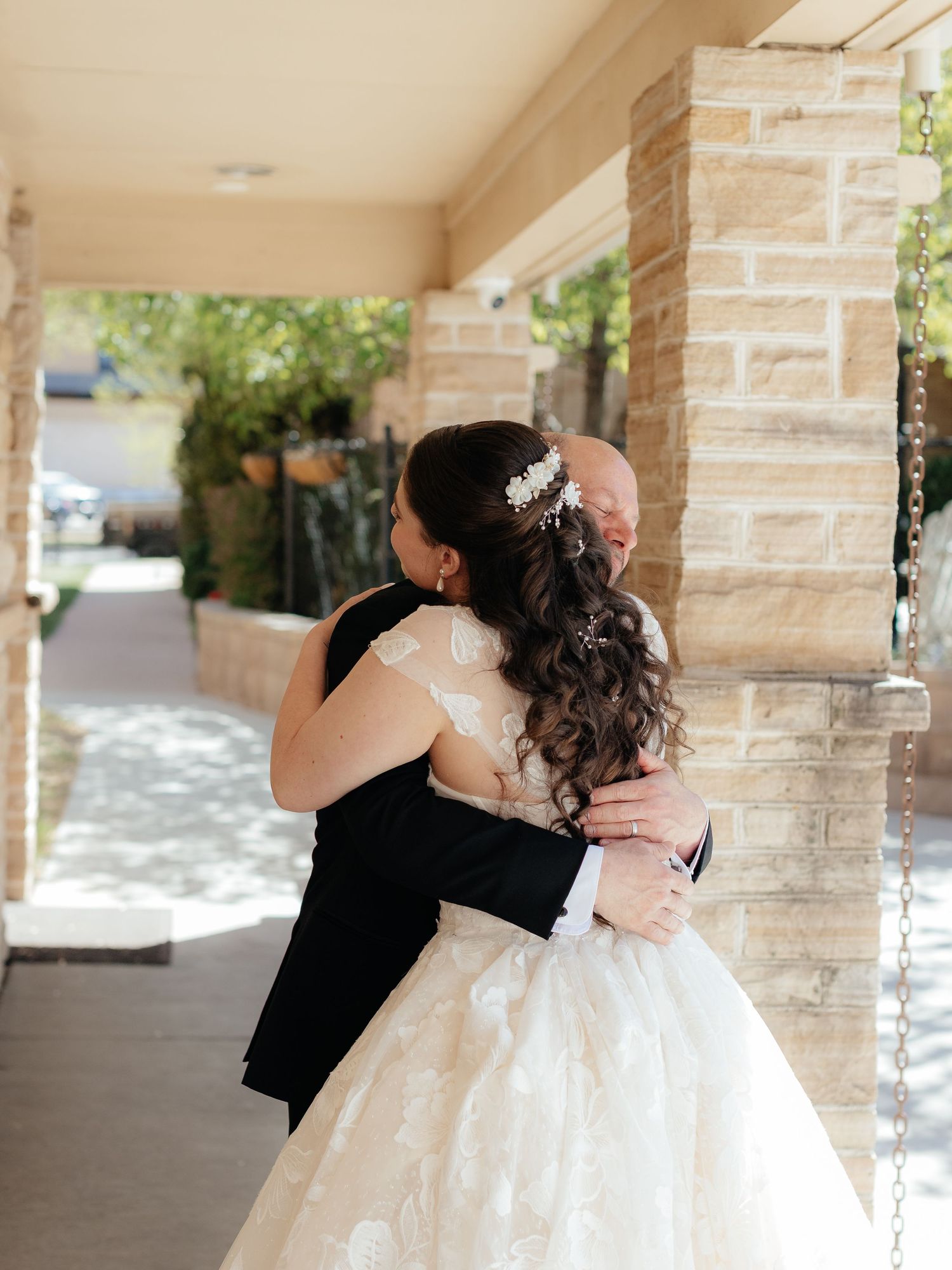 Bride and groom share a tender embrace outdoors, with bride in lace gown and floral hair accessory.