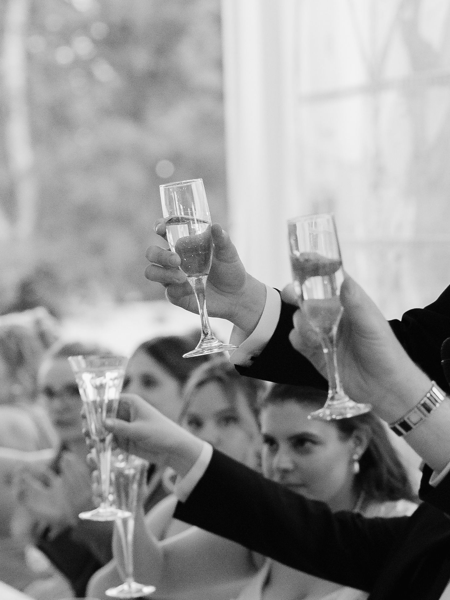 Wedding guests raise champagne glasses in a celebratory toast during reception in black and white.