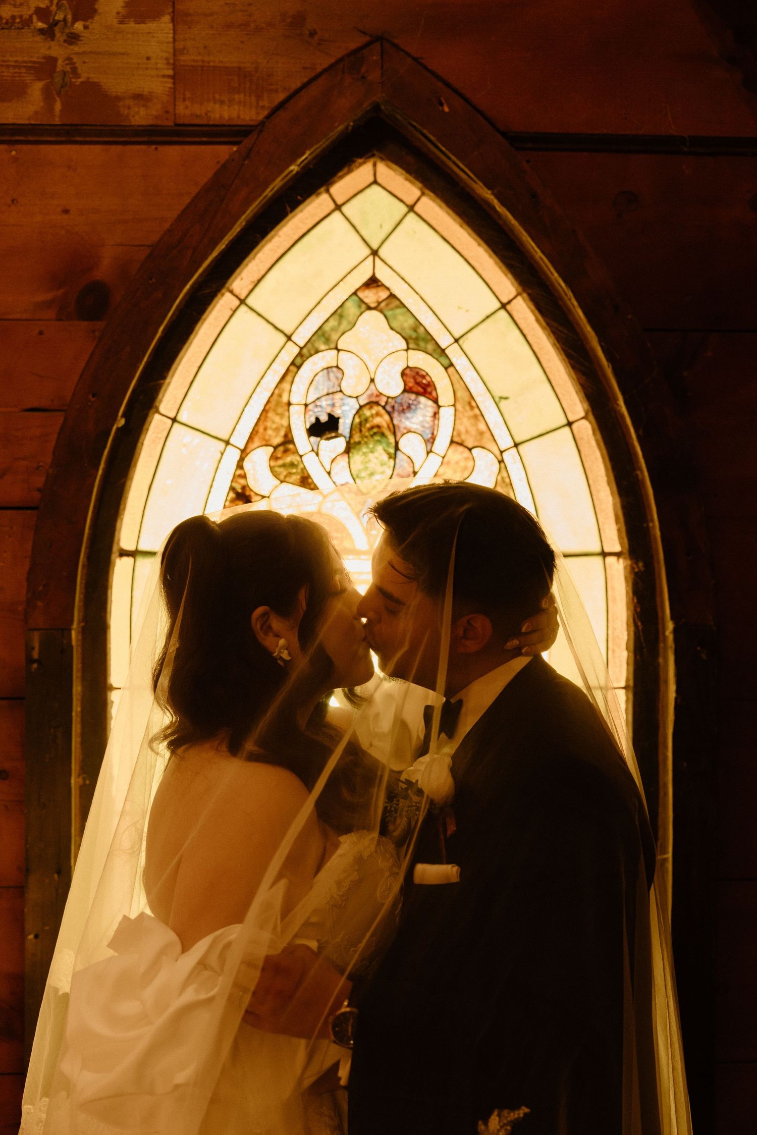A romantic silhouette of a couple embracing in front of an illuminated Gothic church window.