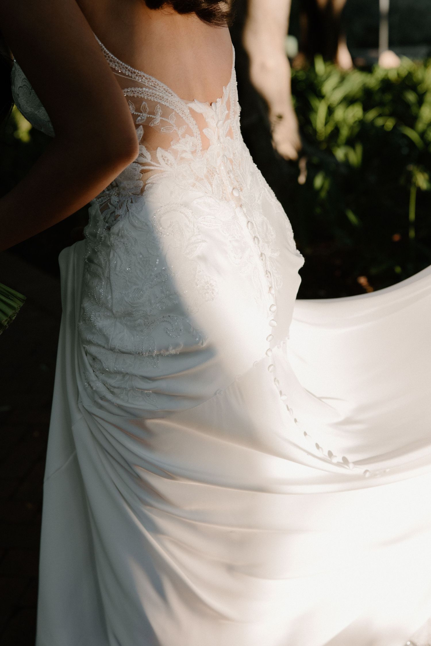 Close-up details of a flowing white wedding dress with delicate lace bodice and satin skirt in natural lighting.