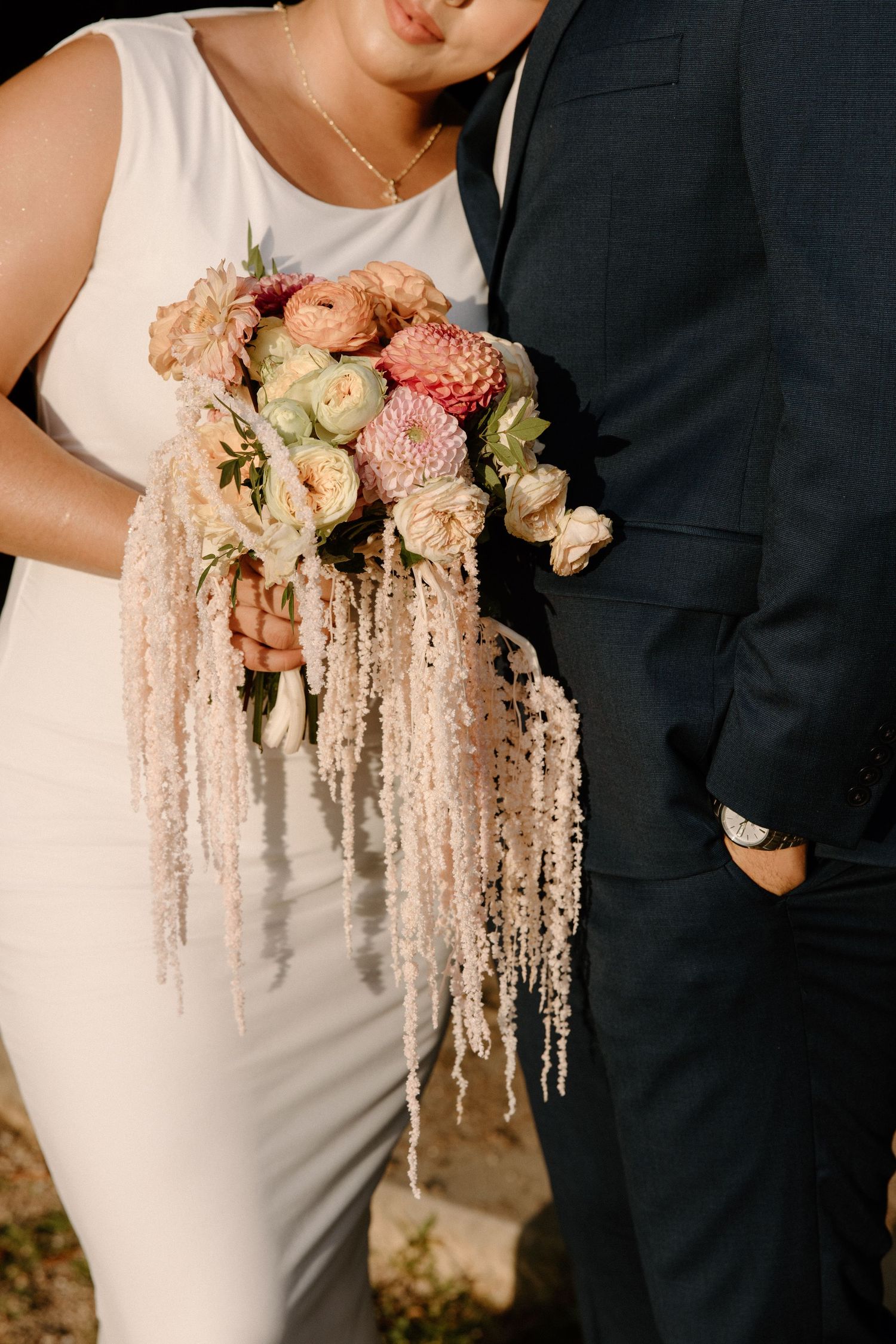 Close-up detail of elegant wedding bouquet with cascading white amaranthus and blush pink flowers against formal attire.