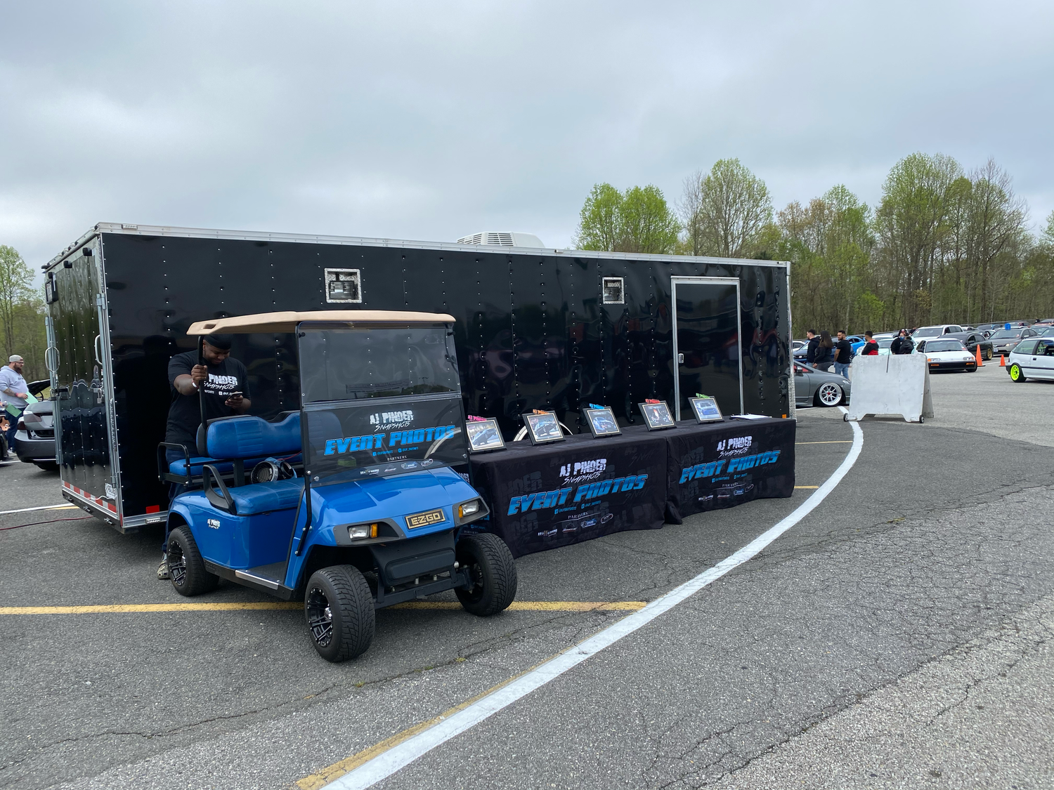 Blue utility vehicles parked beside a black enclosed trailer in a lot.