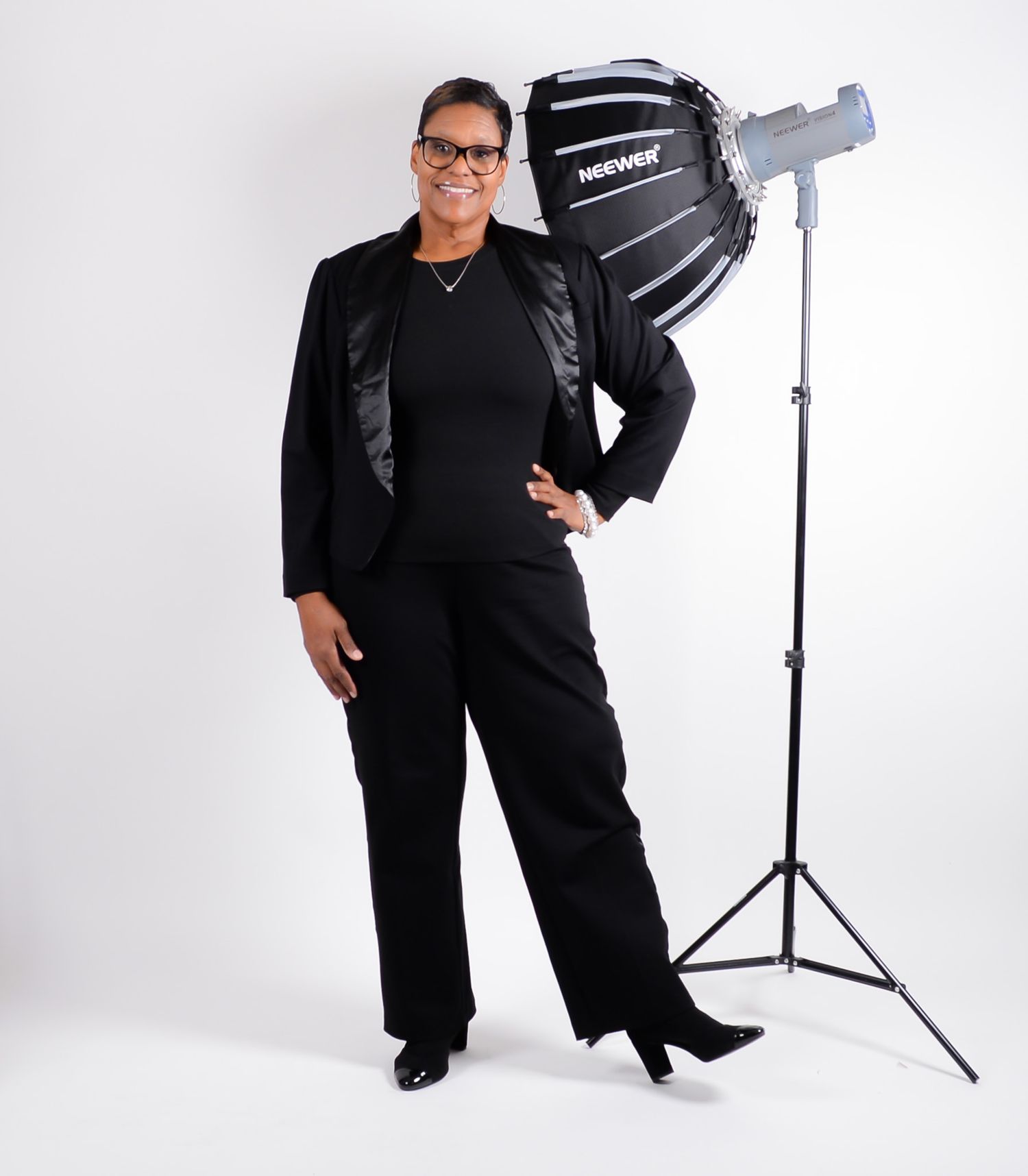 Professional photographer in black outfit posing with studio equipment against white background.