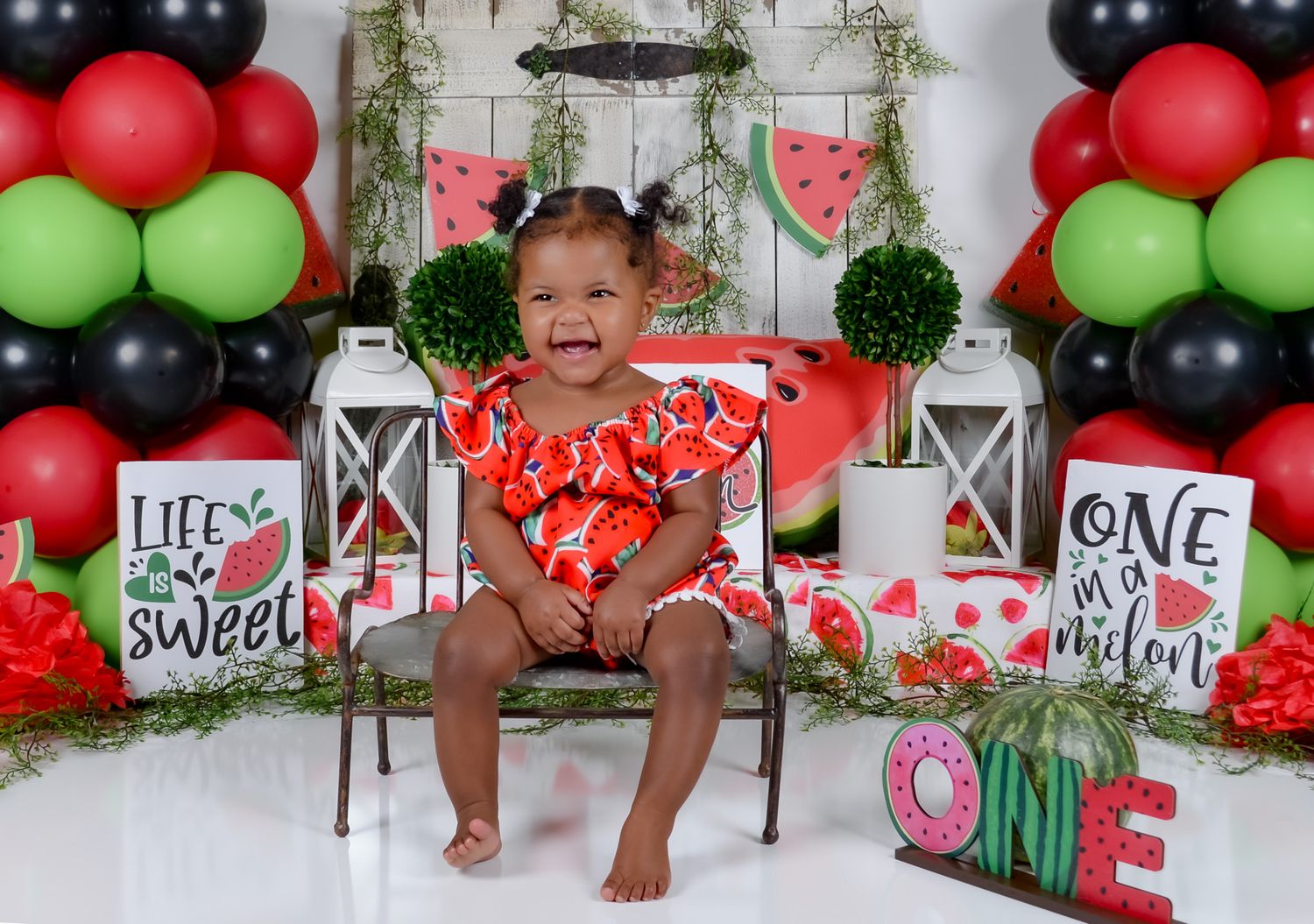 Watermelon themed first birthday setup with balloons, lanterns and decorative signs.