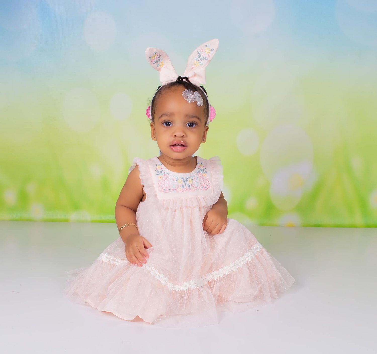 Baby in pink dress sitting against soft green background during professional photo session.