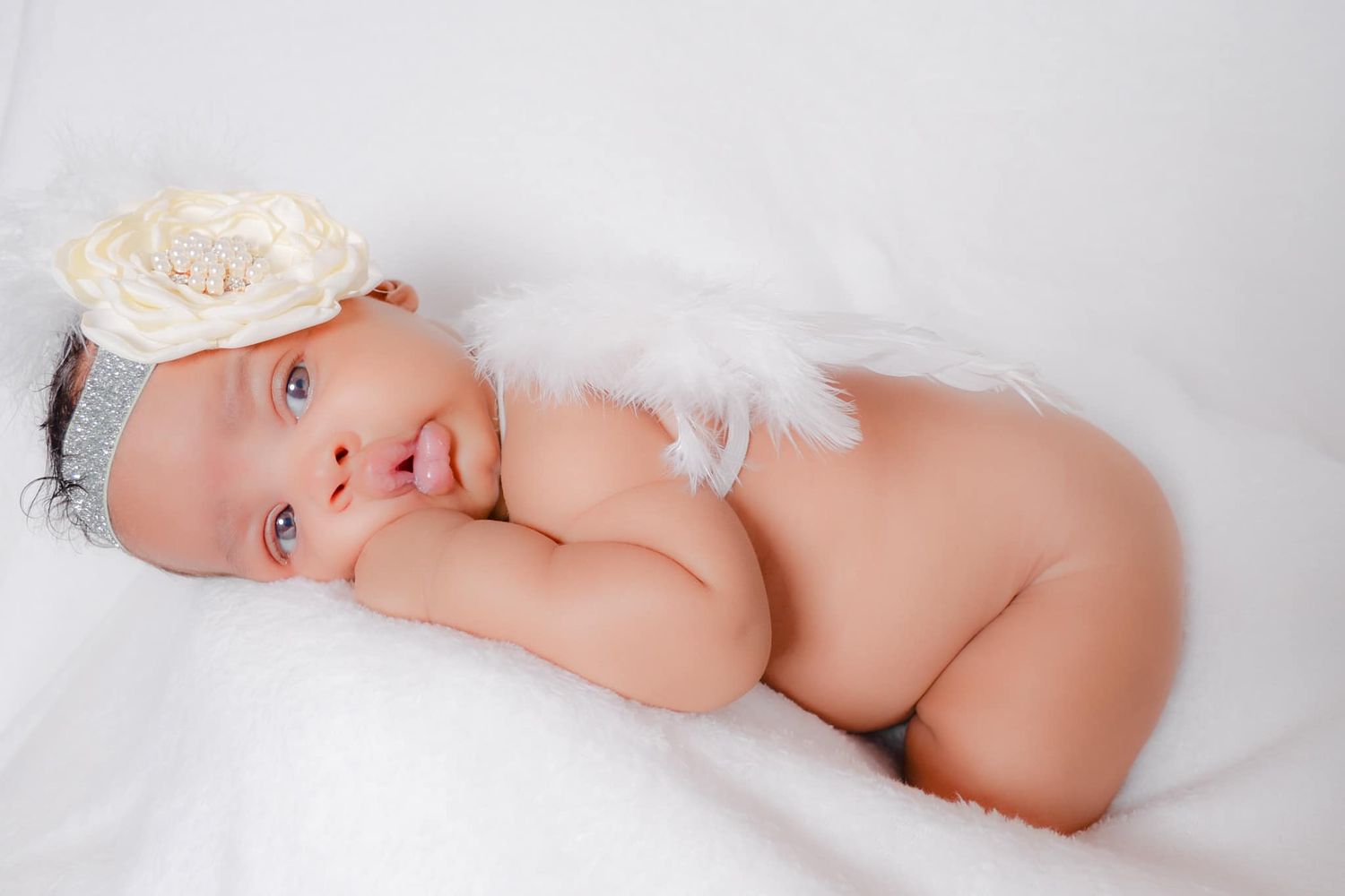Newborn photography with white flower headband and angel wings on white backdrop.