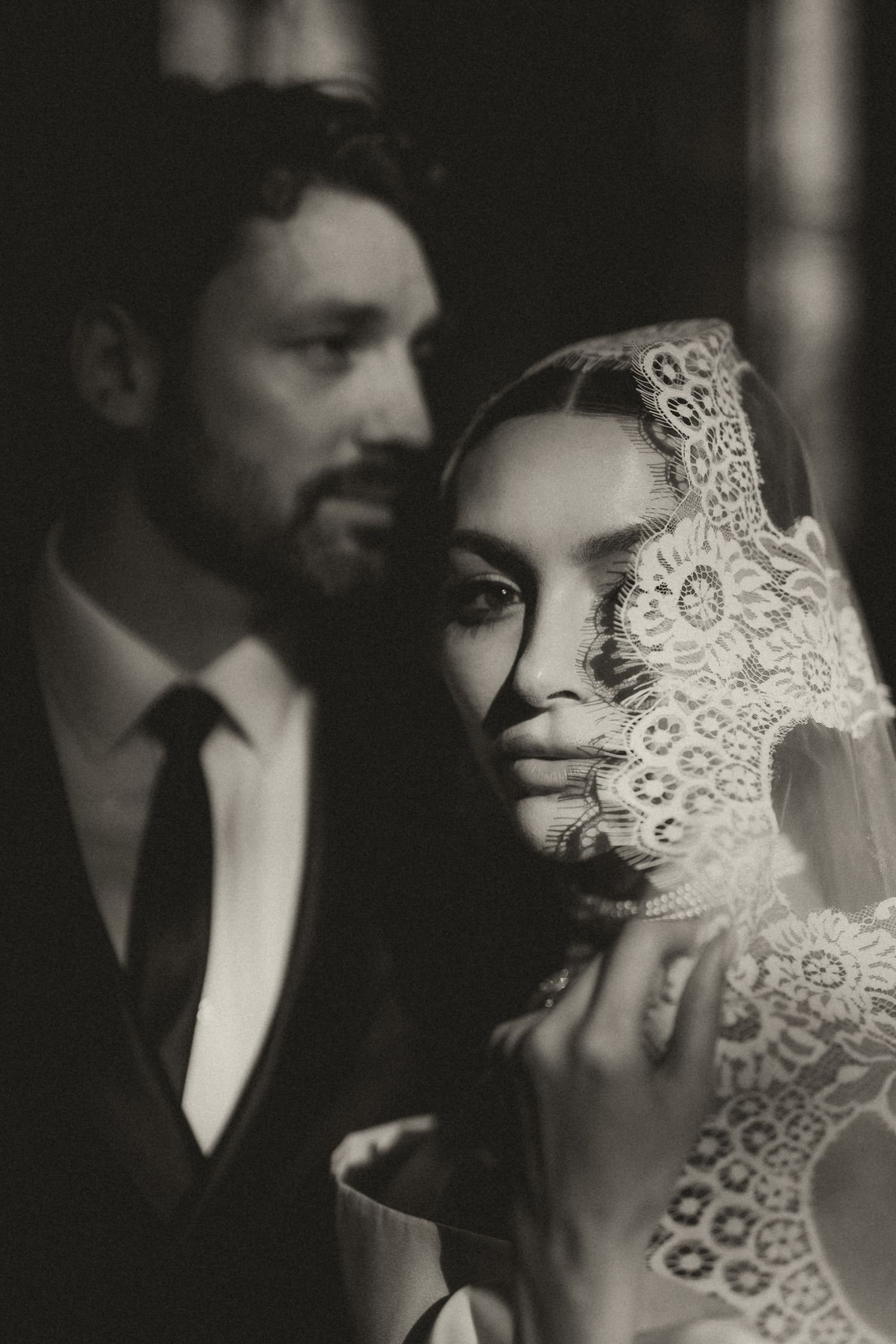 Romantic black and white wedding photo showing couple in intimate pose with delicate lace veil detail.