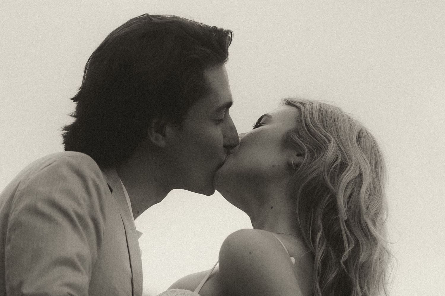 Black and white photo of a romantic couple sharing a tender kiss outdoors in soft natural light.