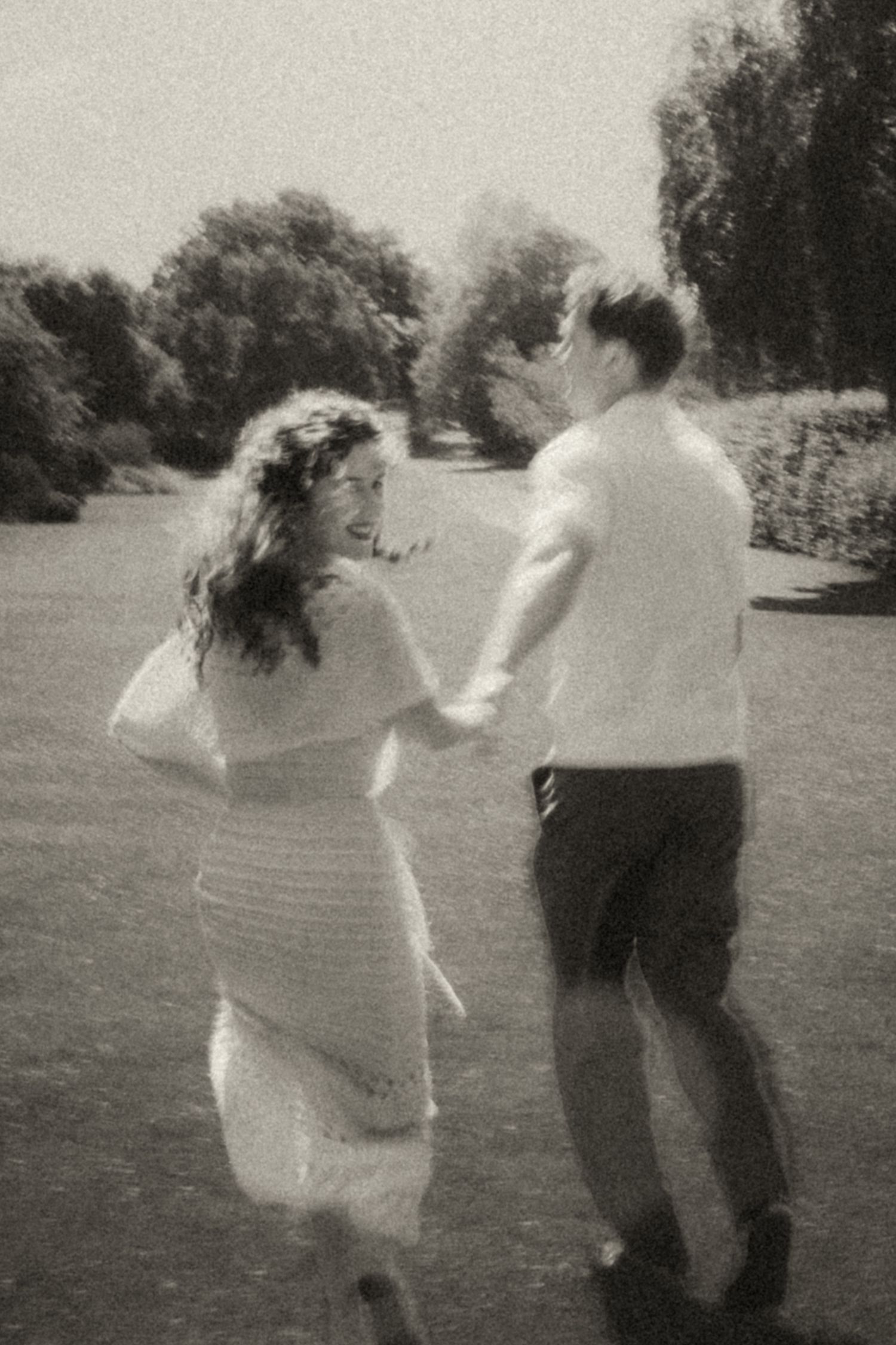 Three people in a field engaged in a playful dance movement sequence captured in black and white photography.